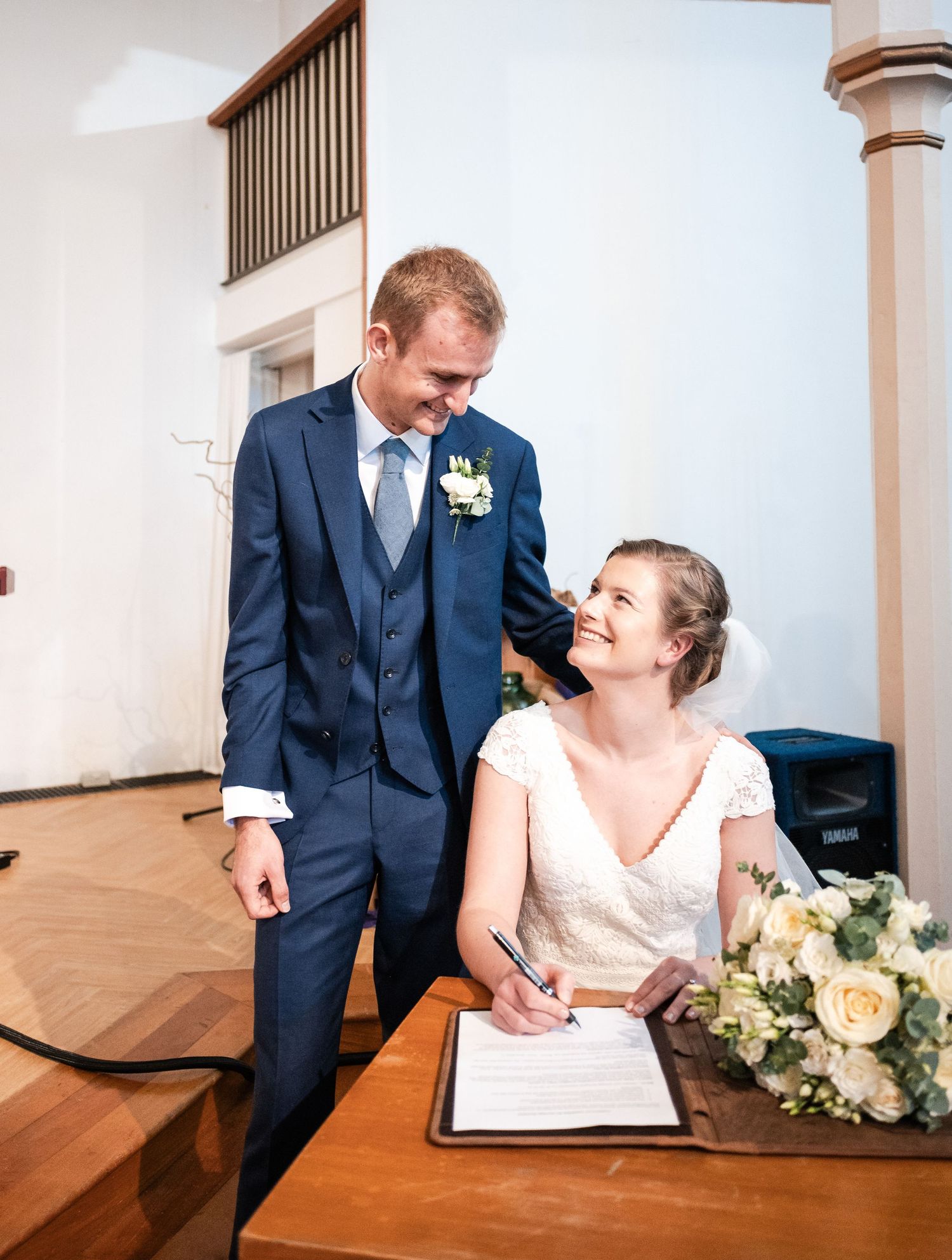 Wedding ceremony signing sequence showing couple at registry table with white floral bouquet and navy suits.