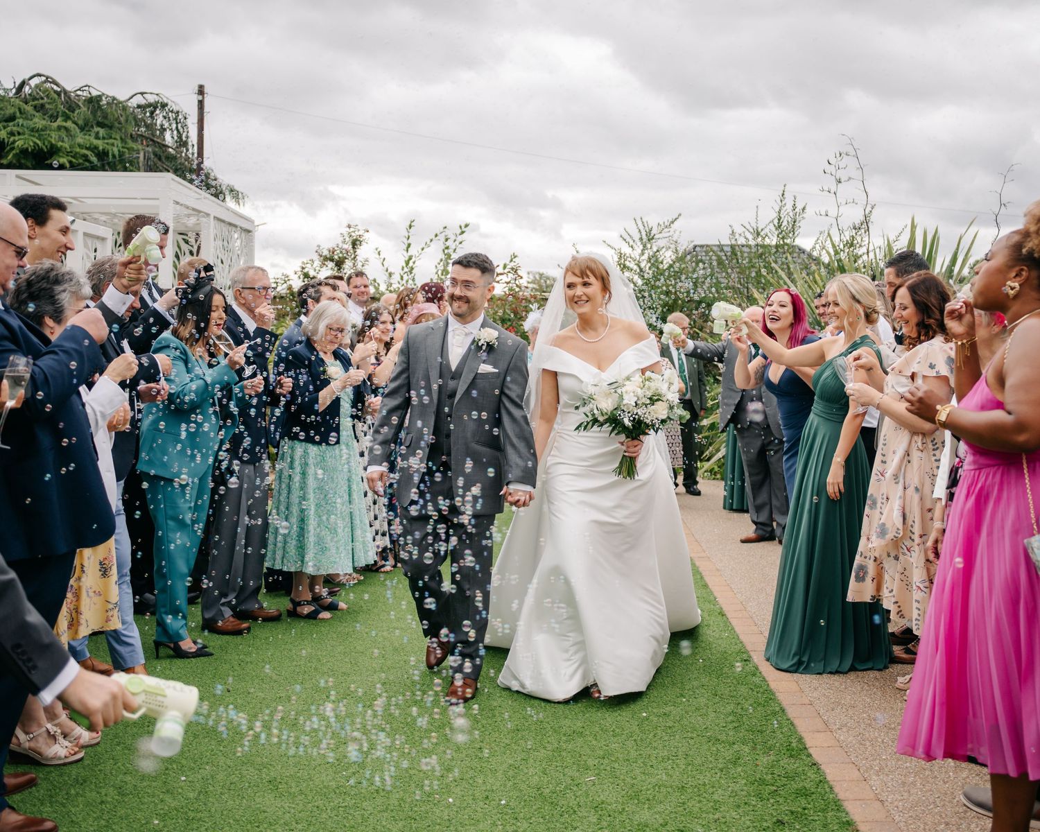 Wedding party and guests gathered on lawn for confetti celebration.