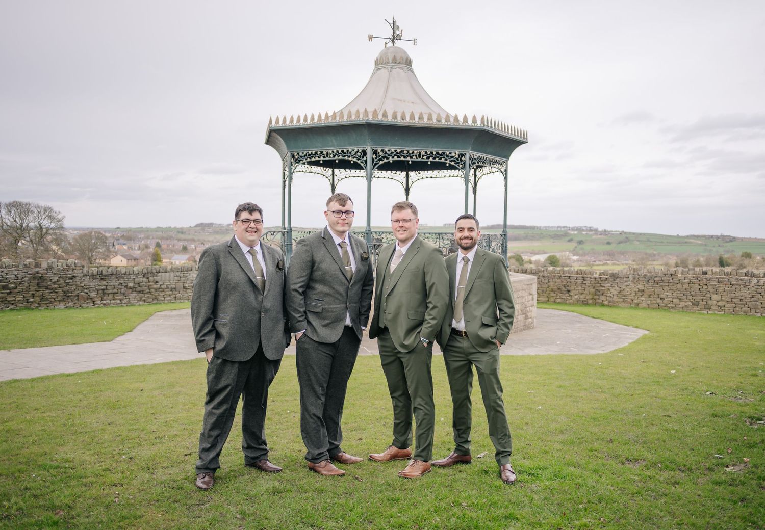 Wedding party in gray suits poses together on a grassy hilltop overlooking a scenic countryside landscape.