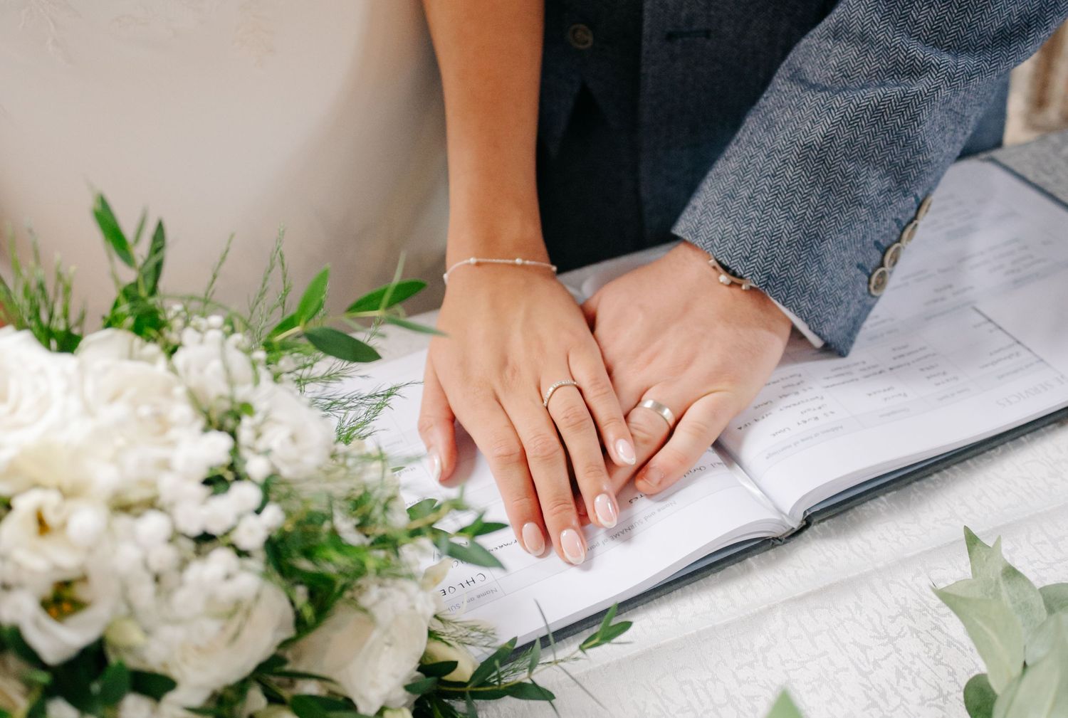Close-up of hands signing wedding documents on white paper.