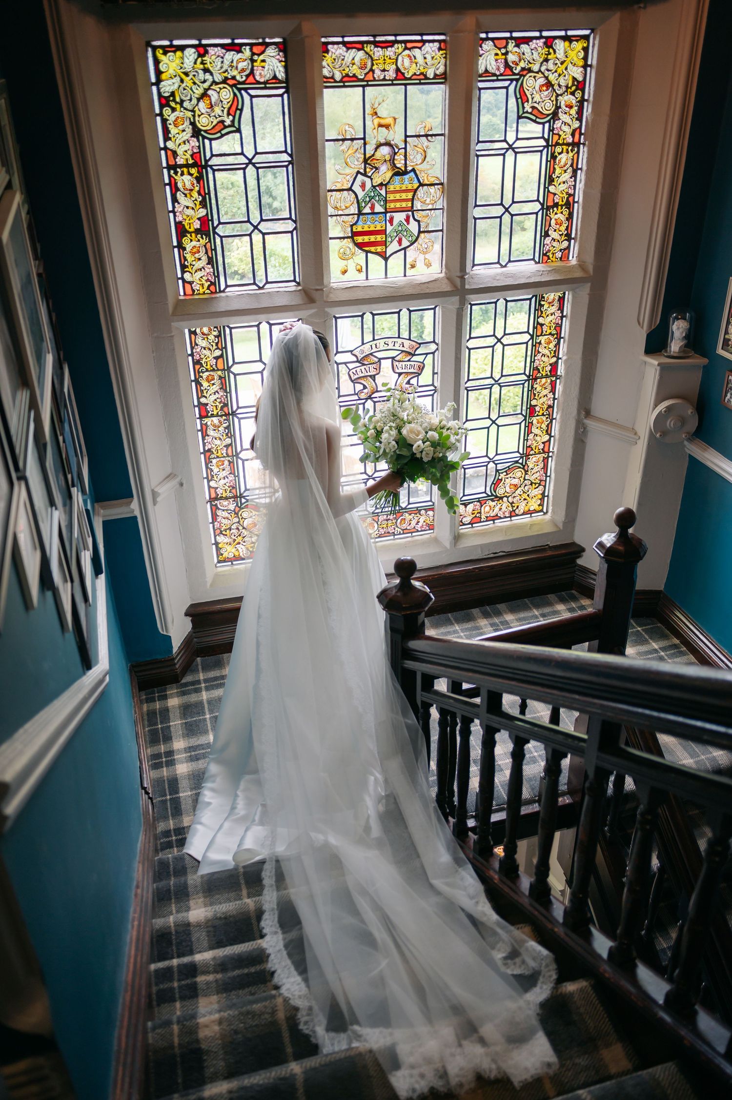 A flowing white wedding veil cascades down a staircase with stained glass windows in the background.