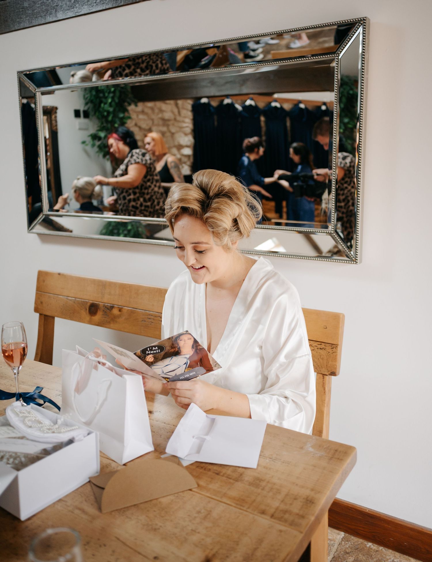 Wedding preparations show a person in white robe writing notes at wooden table with mirrors and decor.