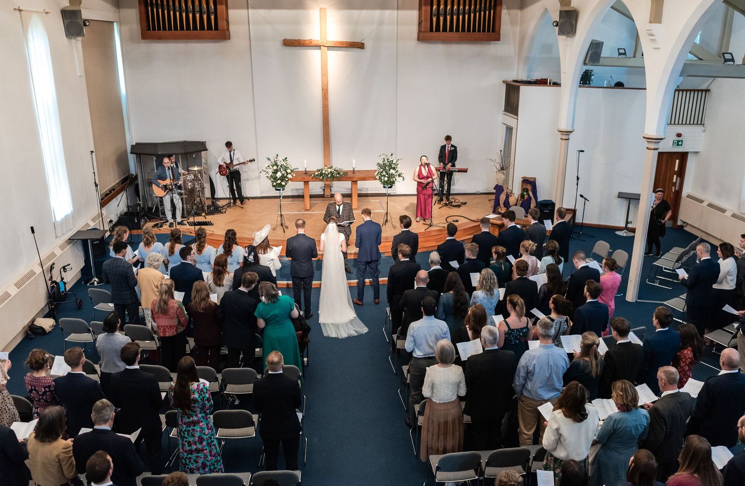 Wedding ceremony in progress inside a modern church sanctuary with guests seated in rows.