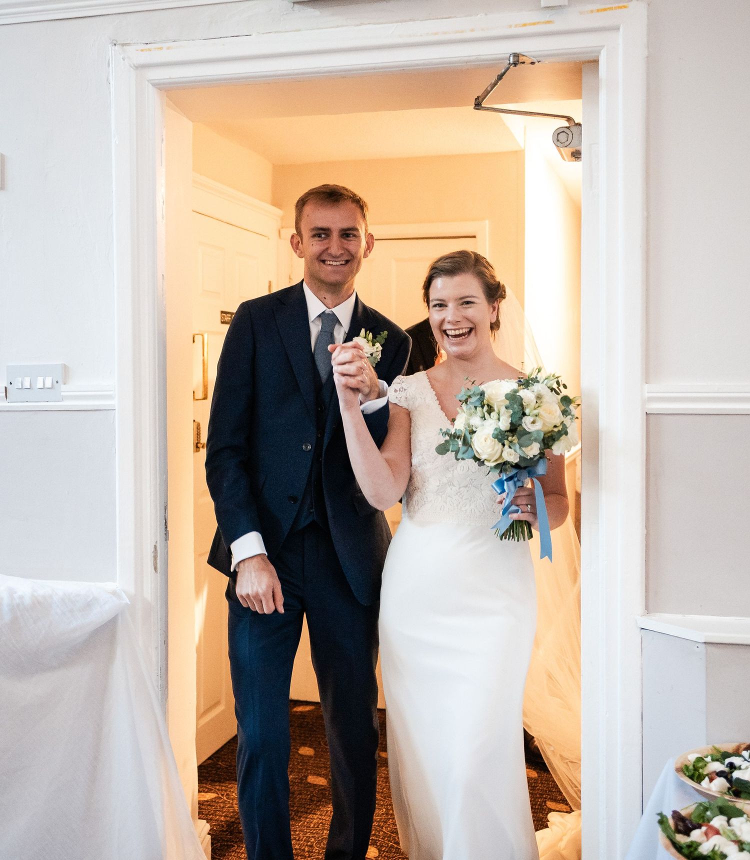 Couple celebrates in a bright white hallway during their wedding day.