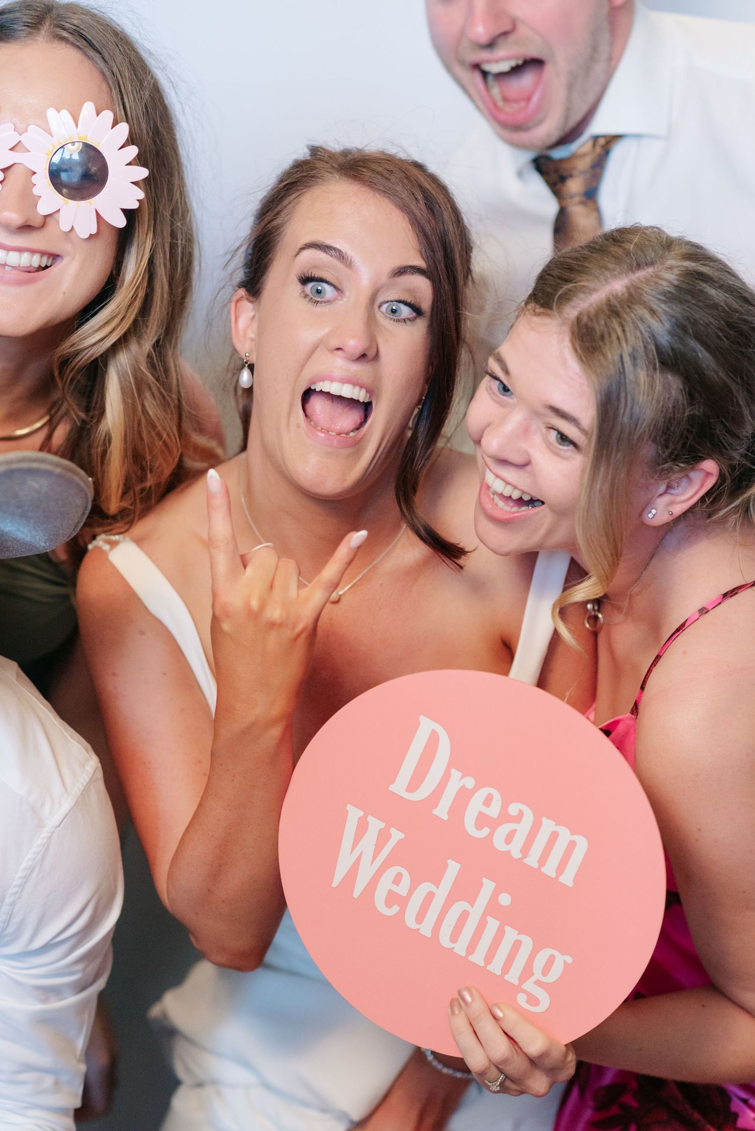 A group of bridesmaids making silly faces while holding pink heart-shaped signs at a wedding celebration.