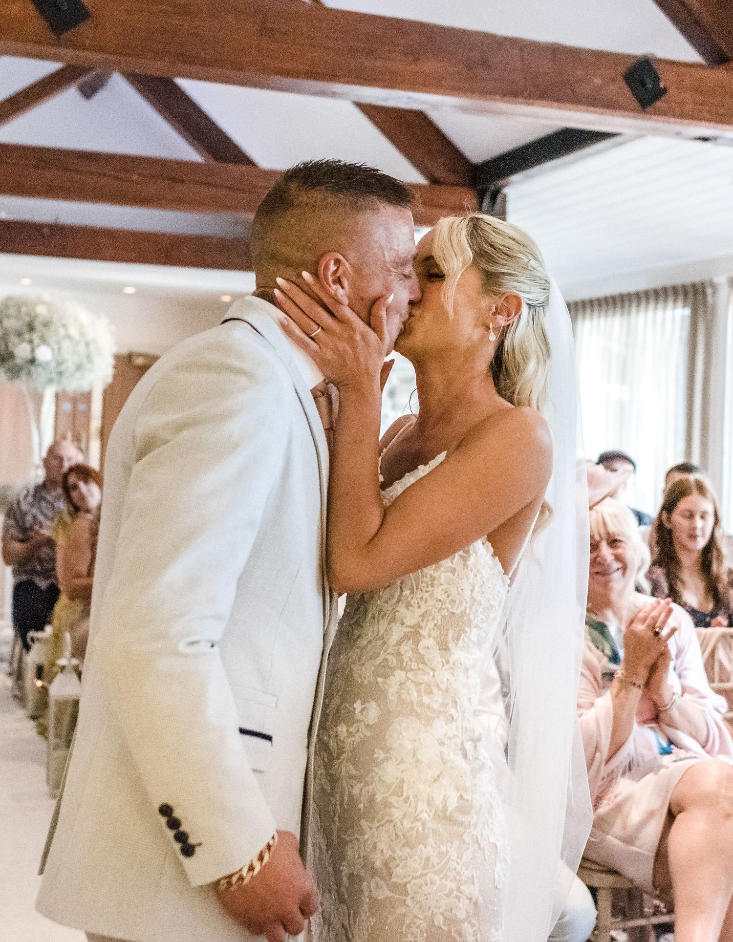 A romantic wedding ceremony kiss in a rustic venue with wooden beams.