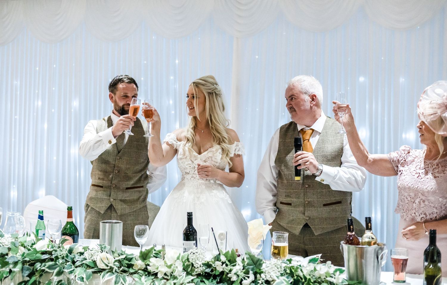 Wedding reception toast moment with guests in formal attire at decorated head table.