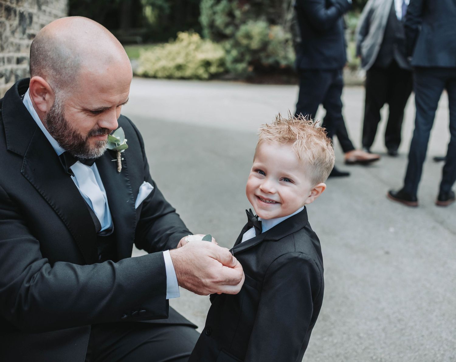 A sweet moment between a suited adult and small child in formal attire on a walkway.