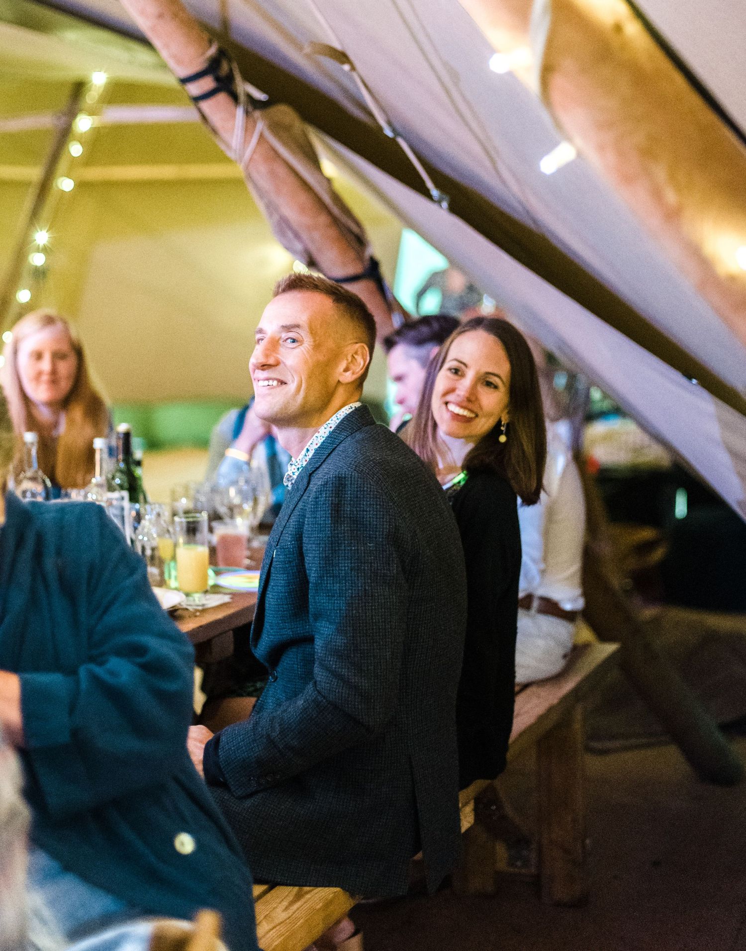 Guests laughing together at a wedding reception table under tent lighting.