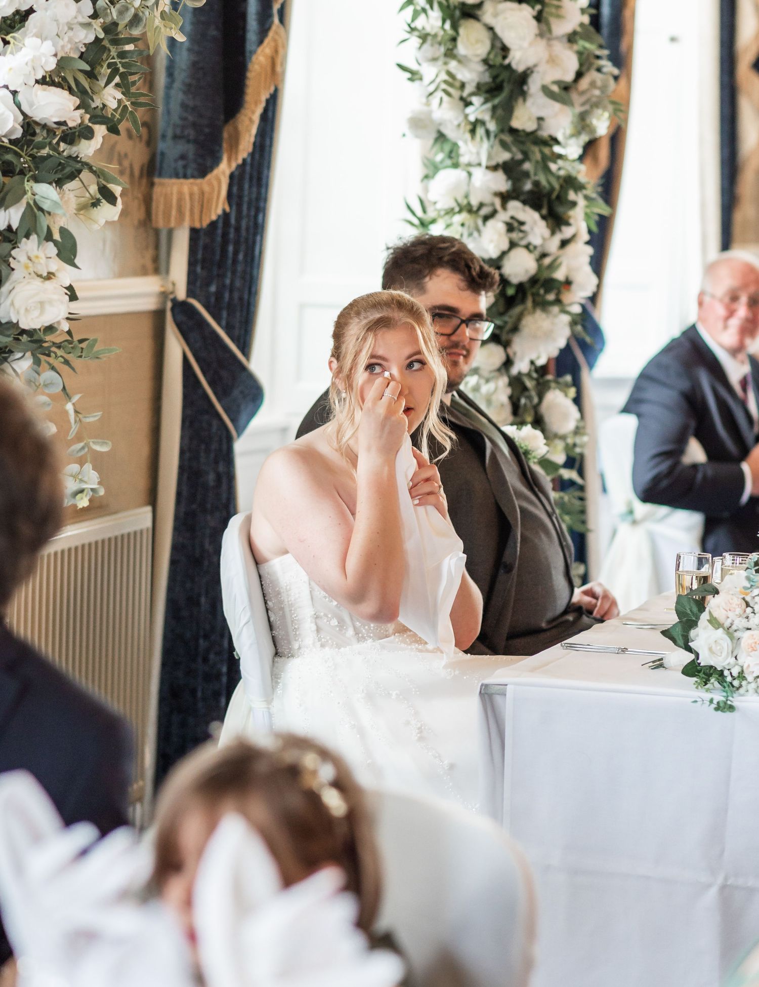 Emotional moment during wedding reception speeches with elegant floral decorations.