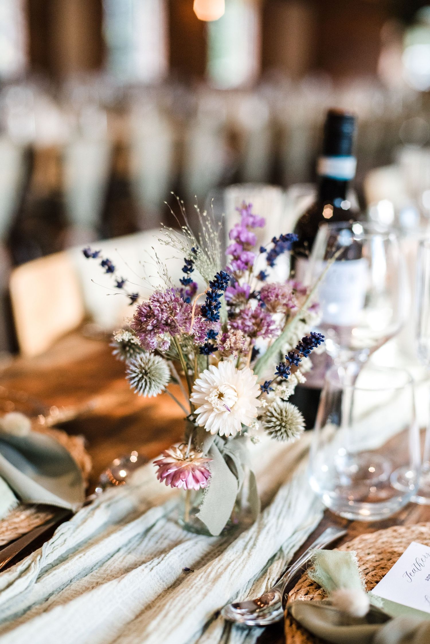 Wedding table centerpiece featuring purple wildflowers, dried flowers and wine glasses.