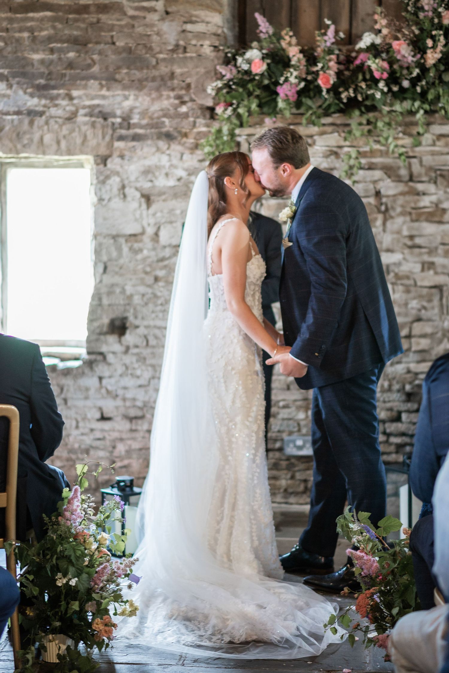 Intimate wedding ceremony moment in rustic stone venue with pink floral arrangements.