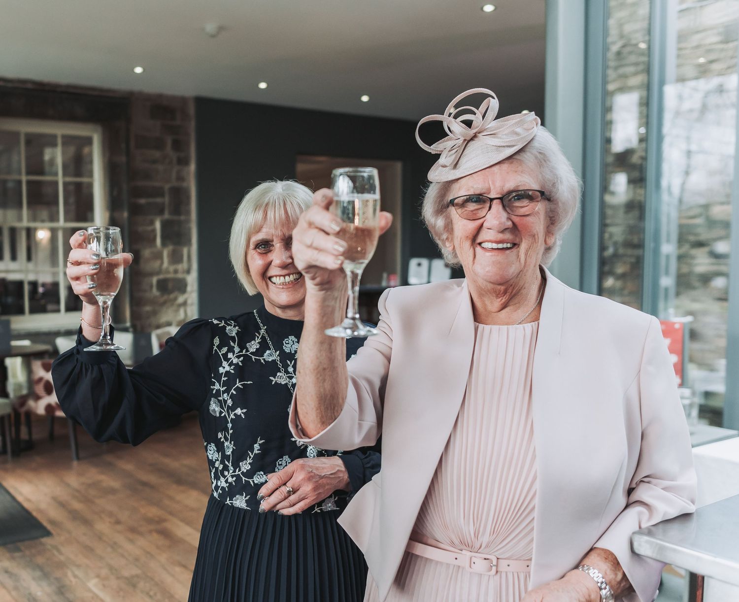 Two elegantly dressed guests in formal attire toast with wine glasses at a celebration.