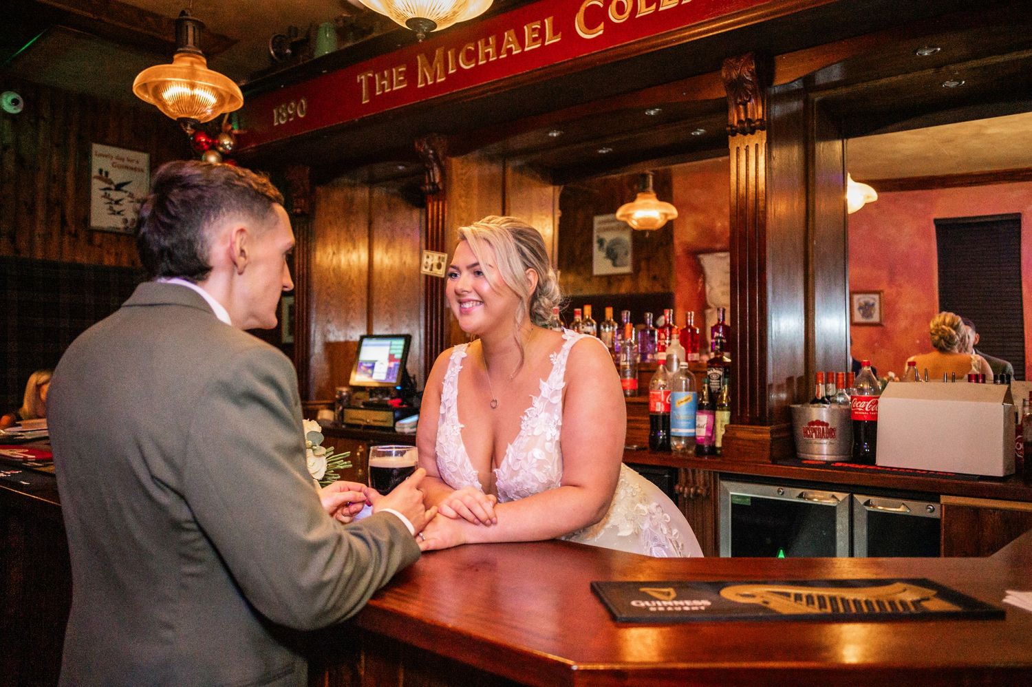 Happy couple shares laughs across wooden bar counter at Irish pub during wedding celebration.