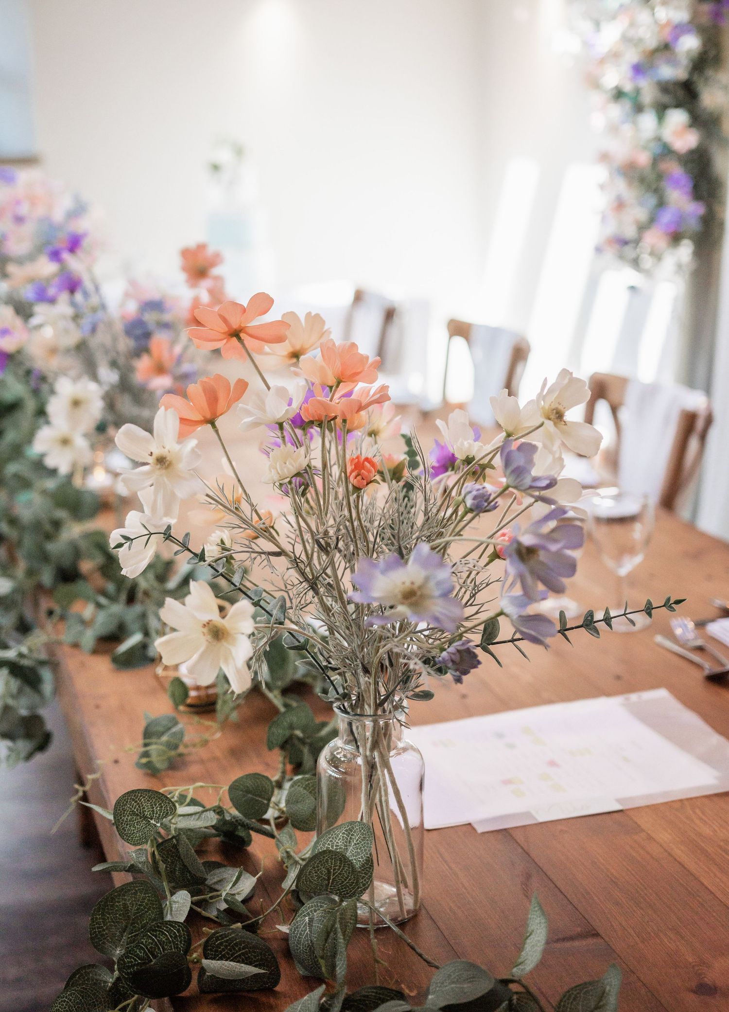 Wildflower centerpiece arrangement with coral and purple blooms on wooden table.