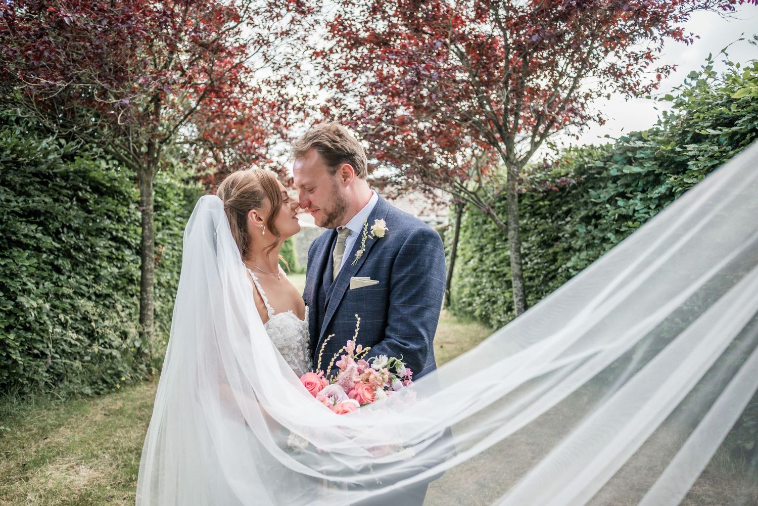 Romantic wedding portrait with flowing veil under canopy of red trees.