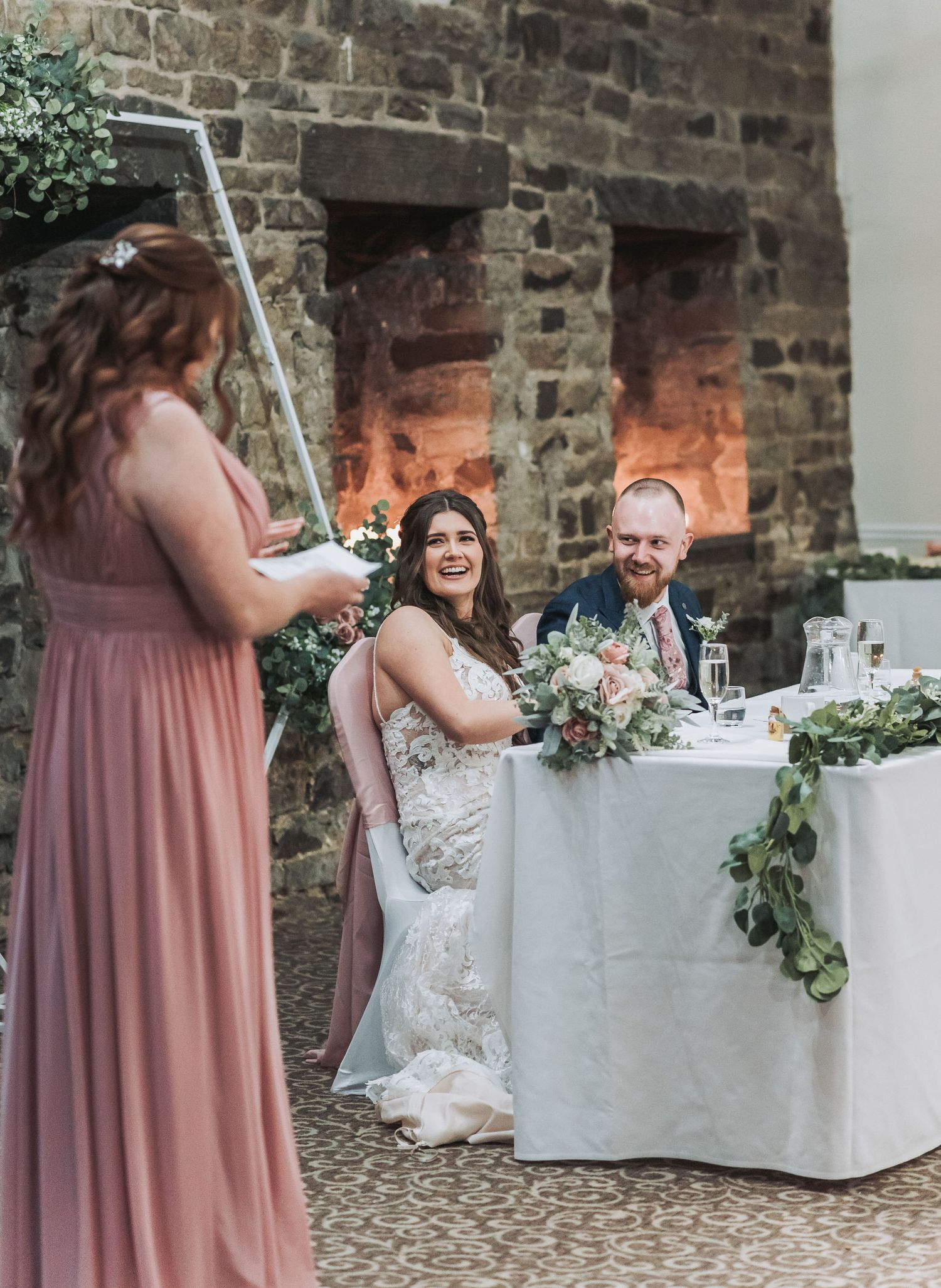 A wedding reception setup with stone walls, floral arrangements and a white tablecloth.