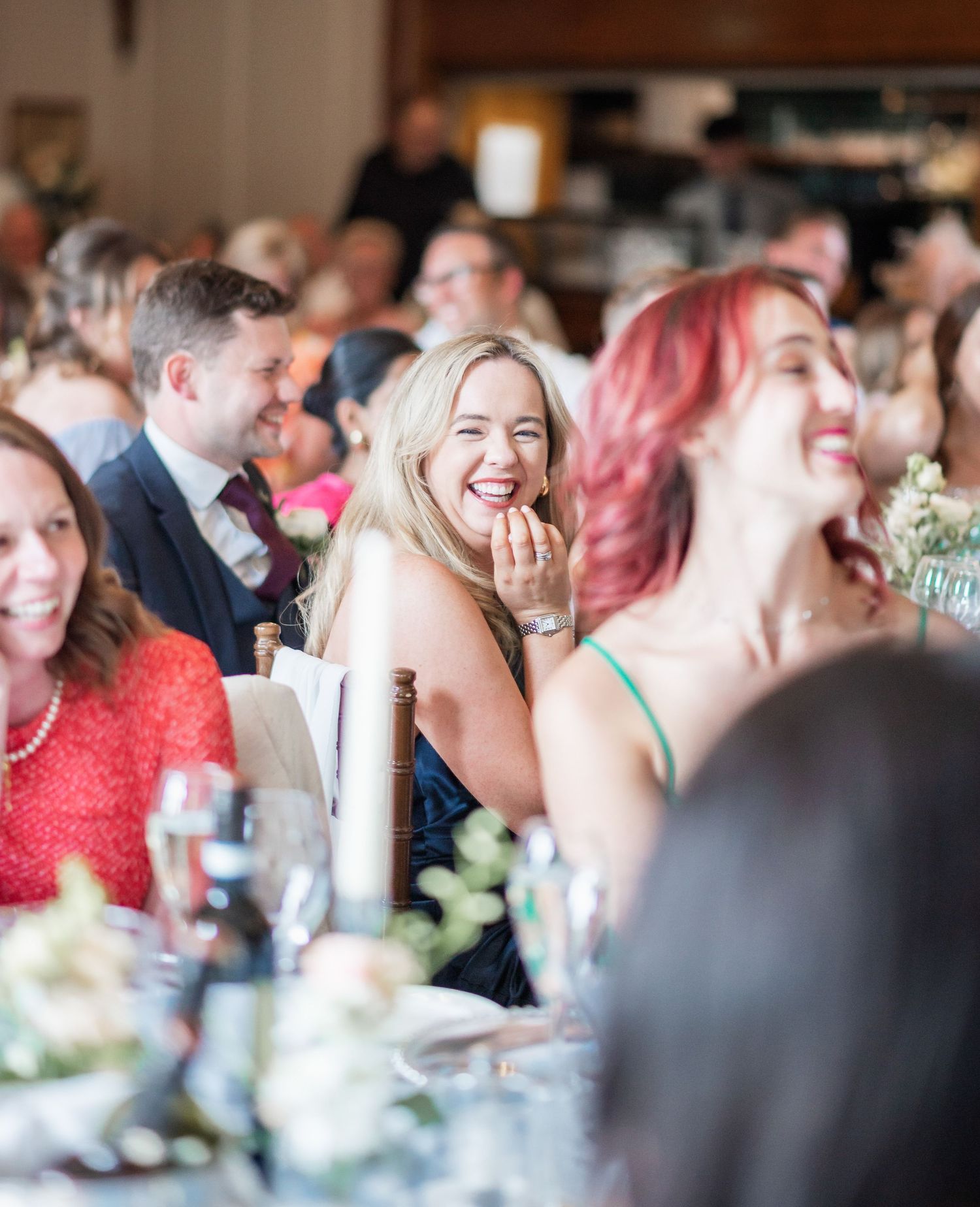 Wedding guests laugh and smile during reception dinner at elegant venue with decorative table settings.