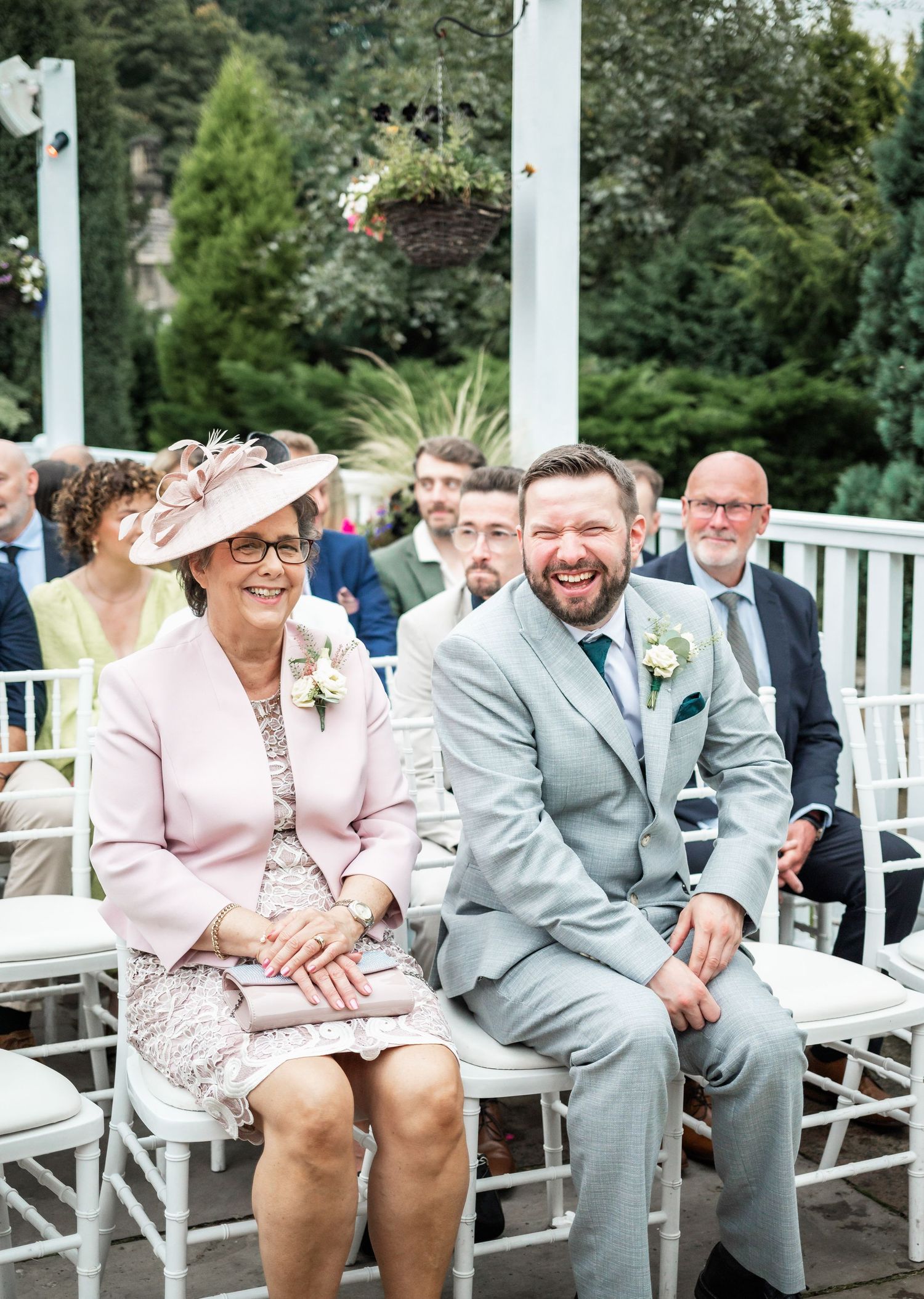 Wedding ceremony guests seated in white chairs at outdoor garden venue.