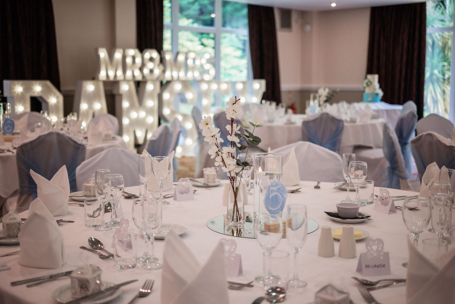 Elegant wedding reception table settings with Mr & Mrs marquee lights and blue accents.