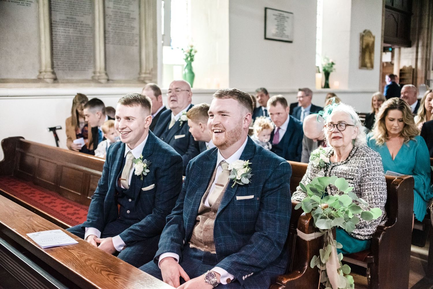 Wedding guests seated in church pews during a ceremony with floral decorations.