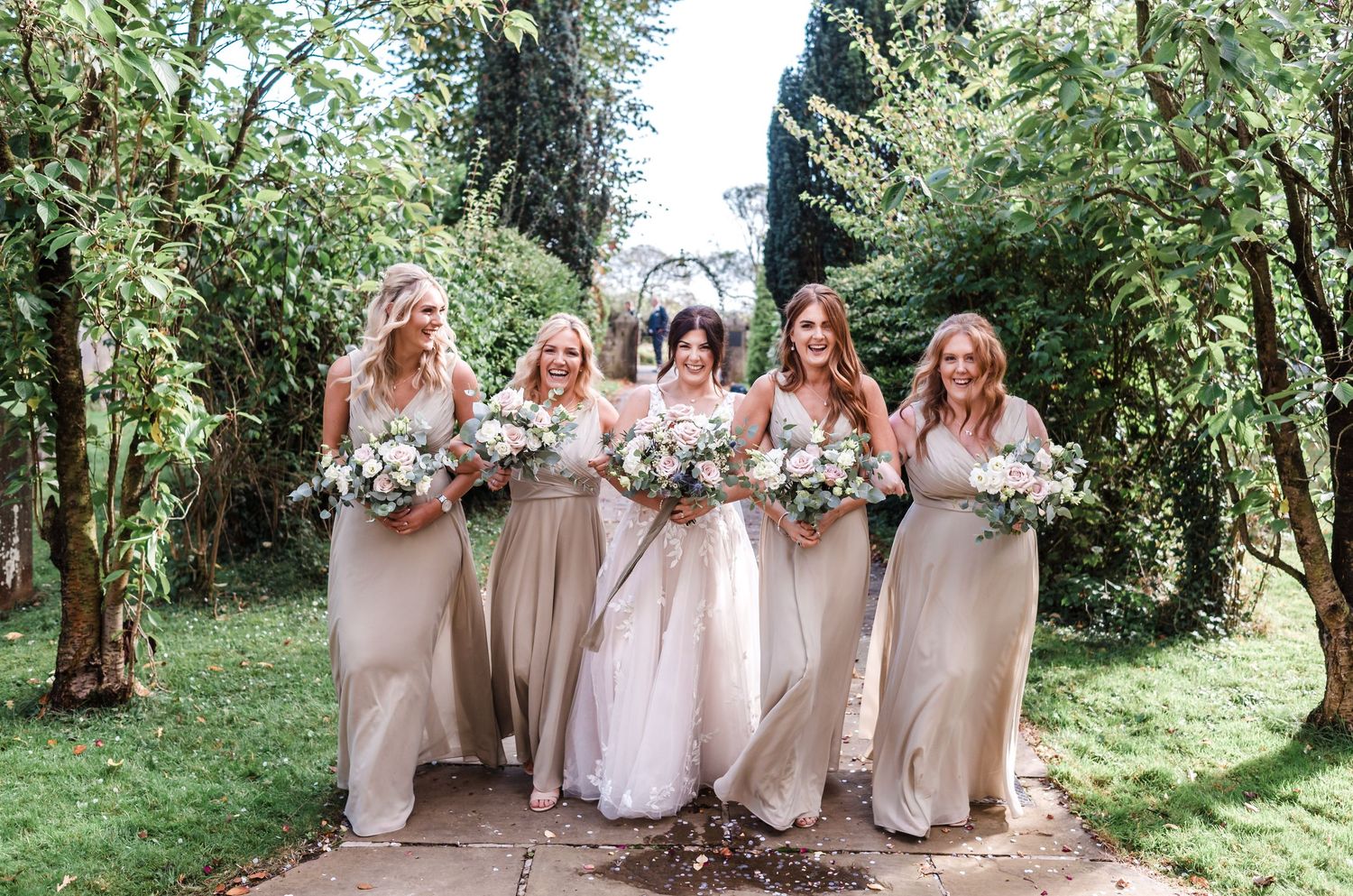 Bridesmaids in neutral dresses posing together in a garden setting.