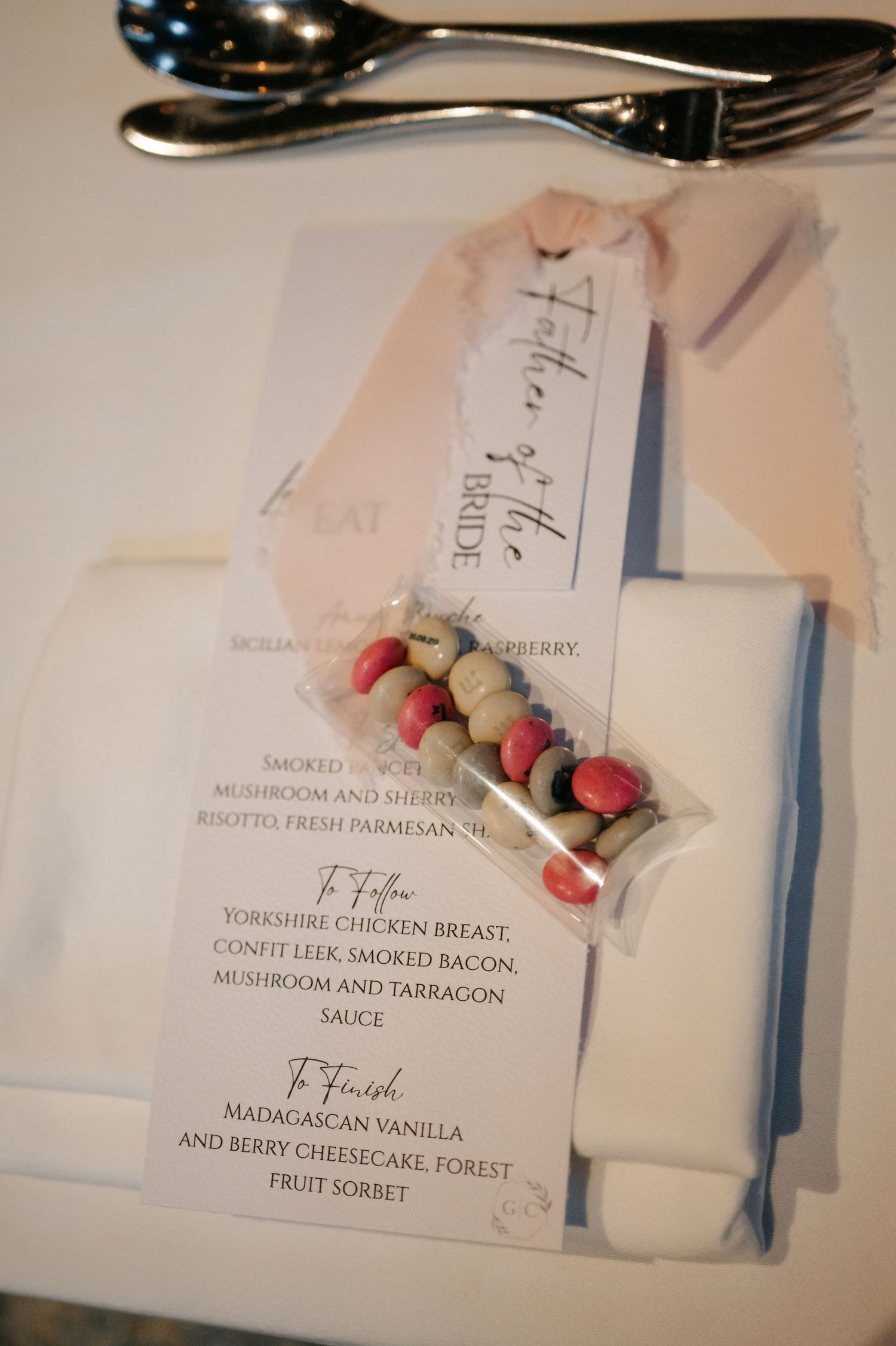 Wedding menu cards with elegant typography displayed alongside silverware on white tablecloth.
