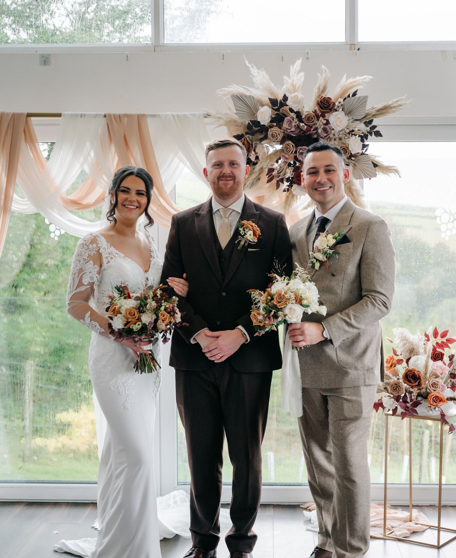 Wedding party poses together in an elegant venue with natural lighting and floral arrangements.