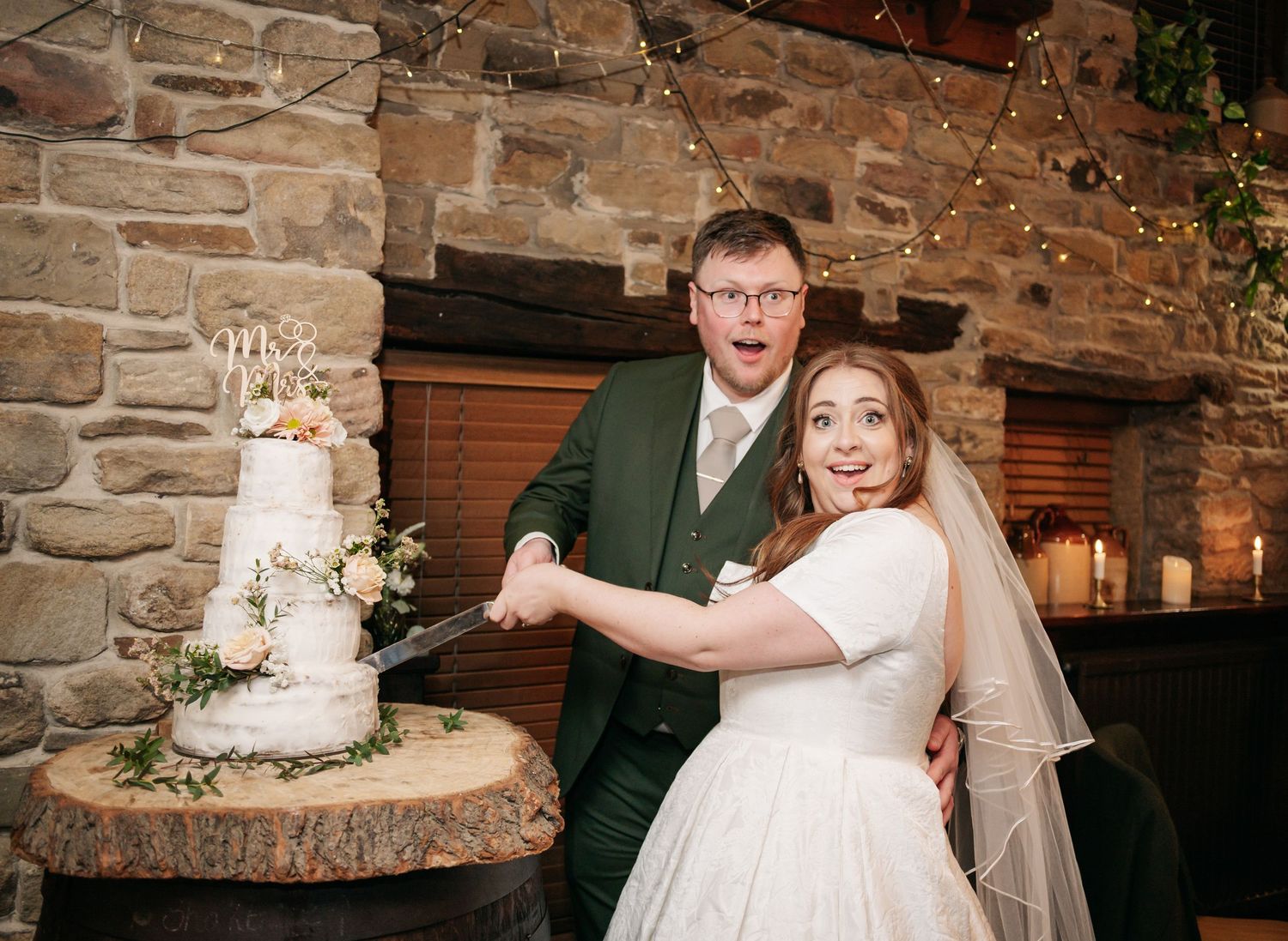 Newlyweds cut their elegant white wedding cake decorated with fresh flowers.