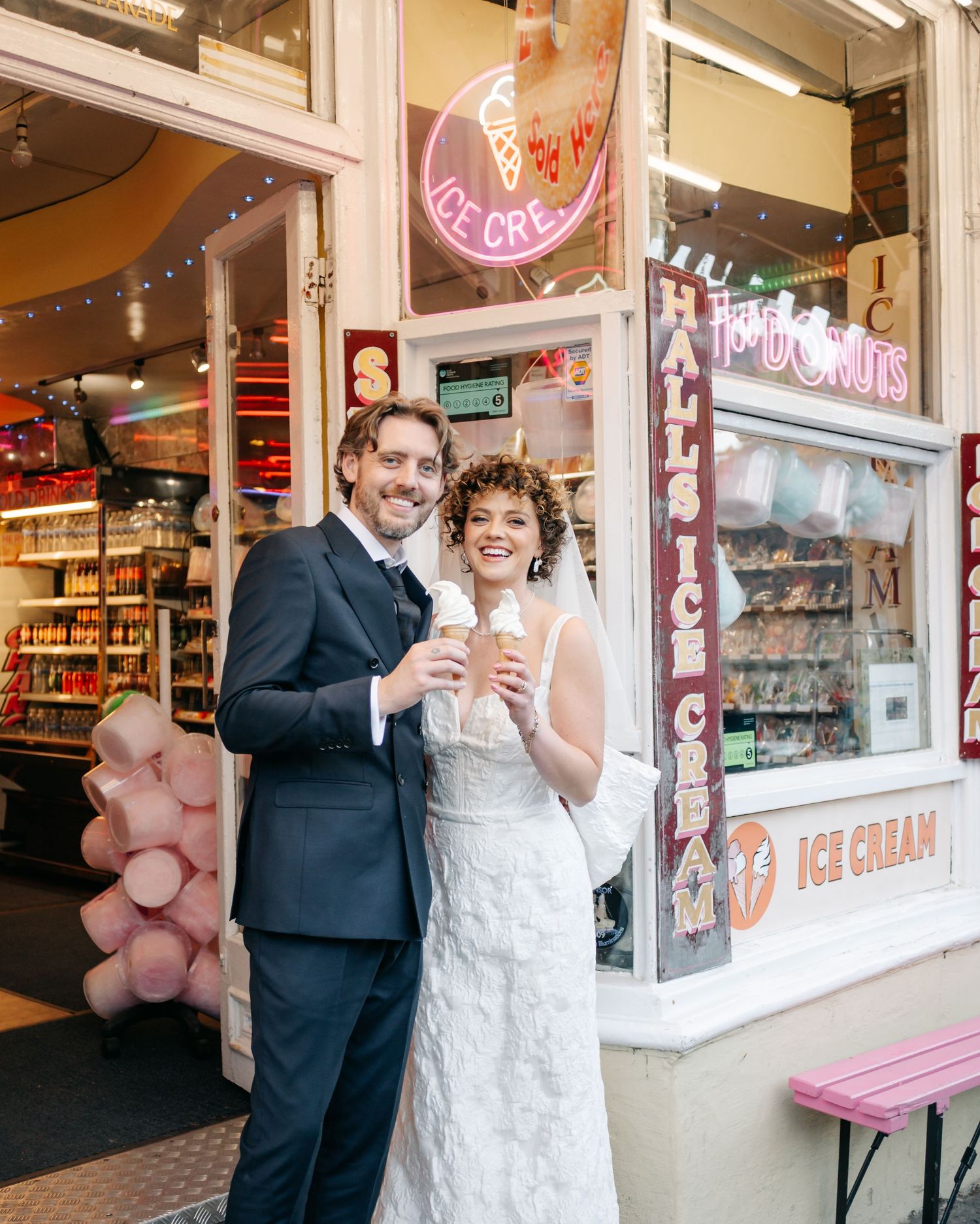 Wedding couple visits an ice cream shop storefront with vintage signage and pink decorations.
