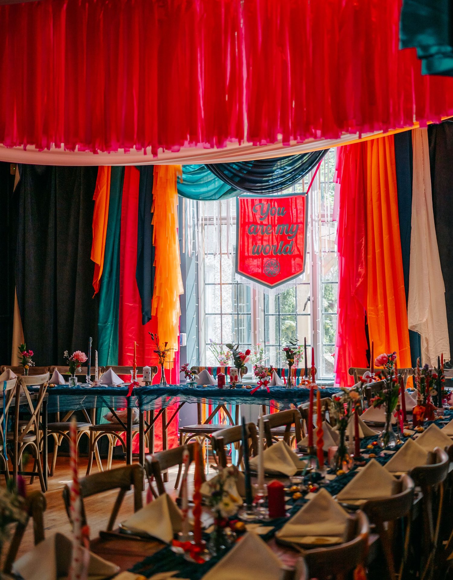 Wedding reception venue with dramatic red and orange draped ceiling and elegant table settings.