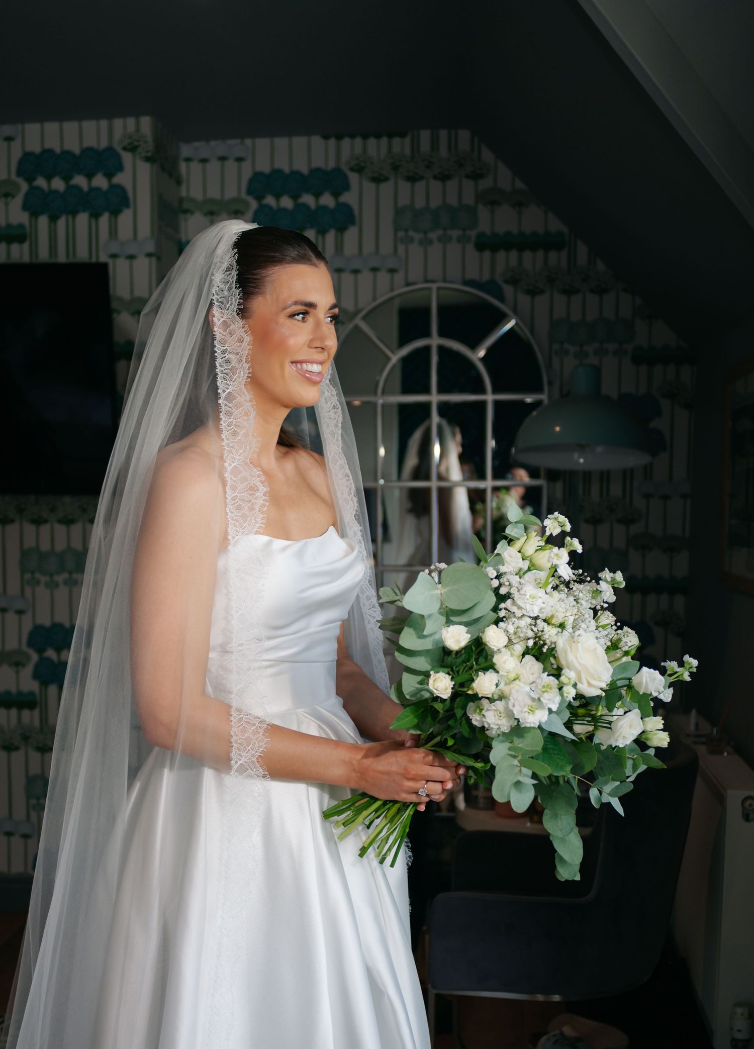 A bride in a classic white wedding gown holds an elegant white floral bouquet with cascading greenery.