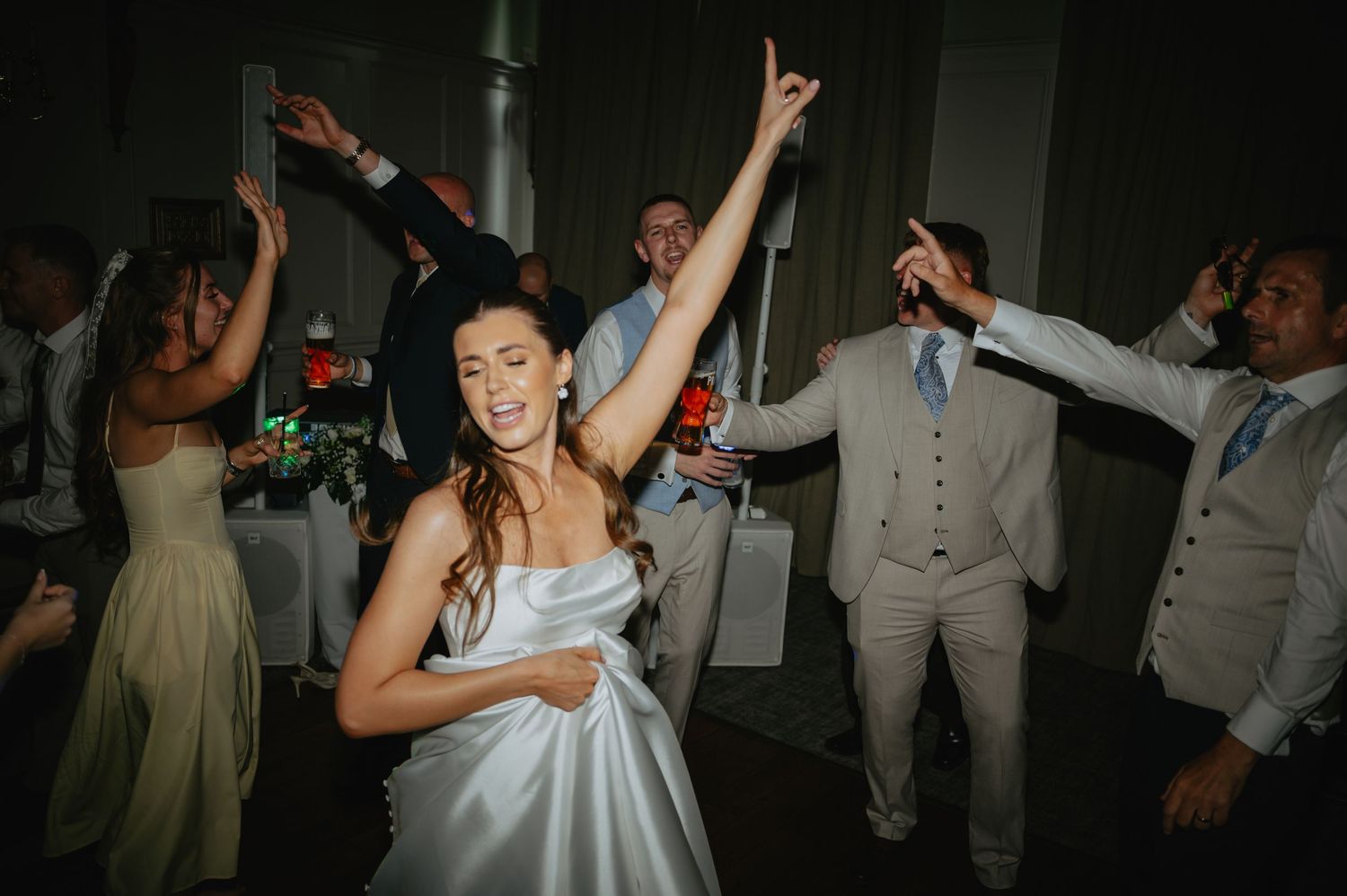 Wedding reception dance party with dramatic lighting and raised hands.