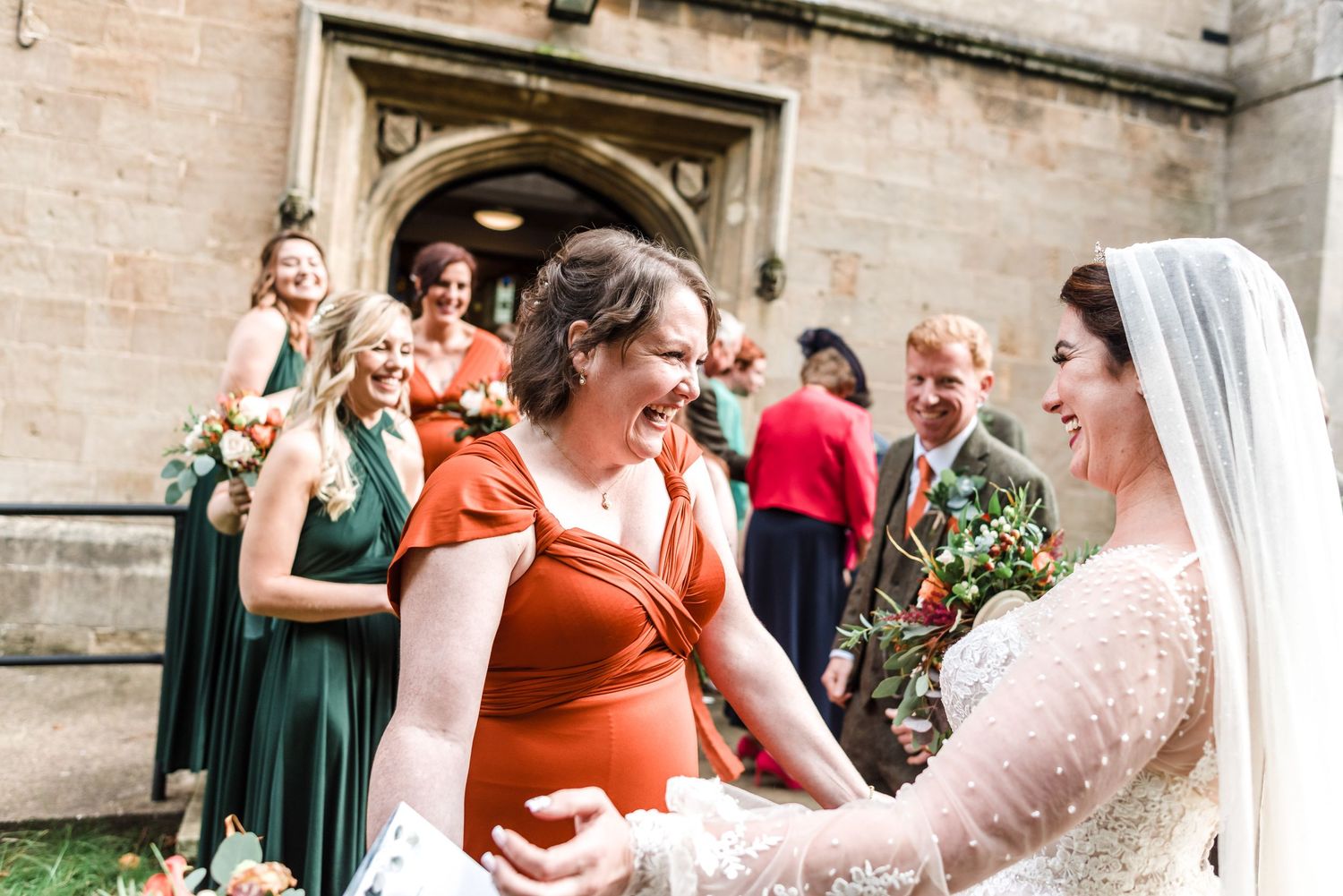 Guests celebrate with the bridal party outside a stone church on a wedding day.