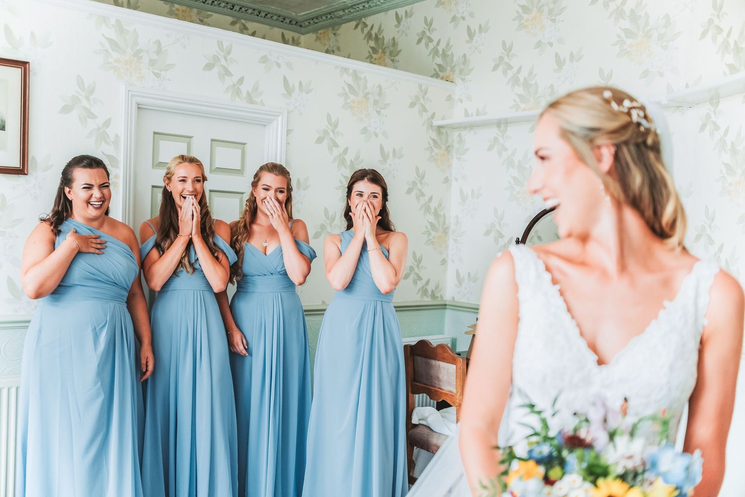 Bridesmaids in light blue dresses react emotionally to seeing bride in wedding gown.