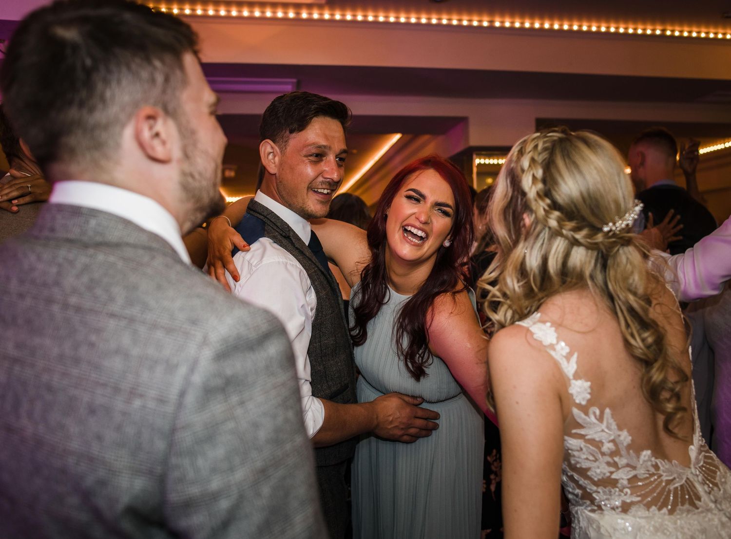 Wedding reception guests dancing and celebrating under warm lighting.