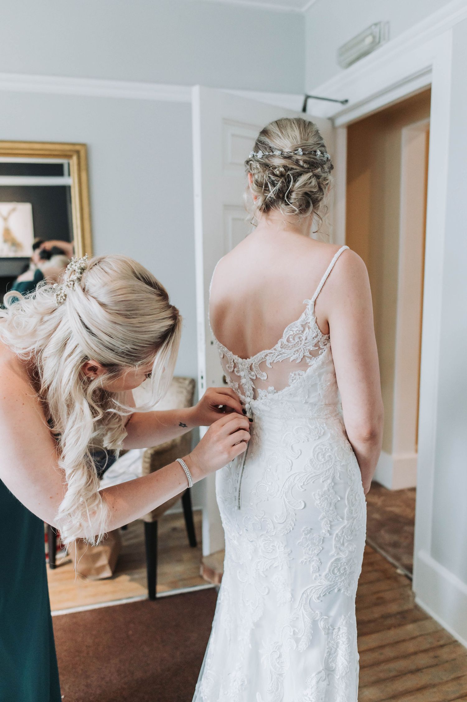 A wedding dress being buttoned up from behind, showing intricate lace detail and elegant styling.