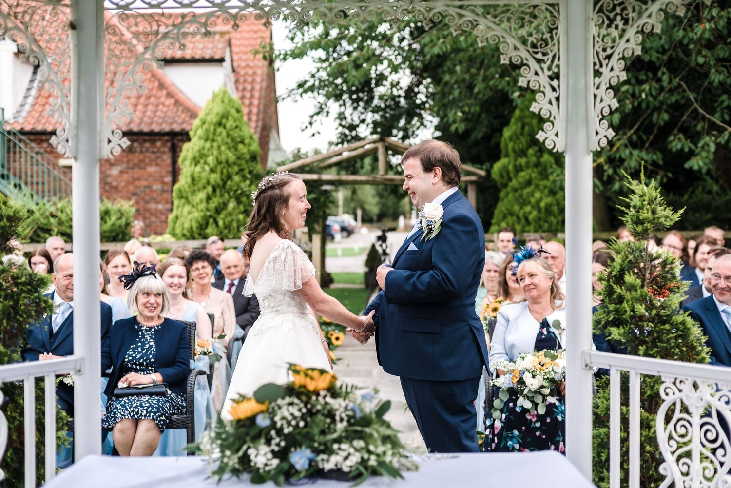A joyful wedding ceremony moment captured under a white gazebo with guests in attendance.