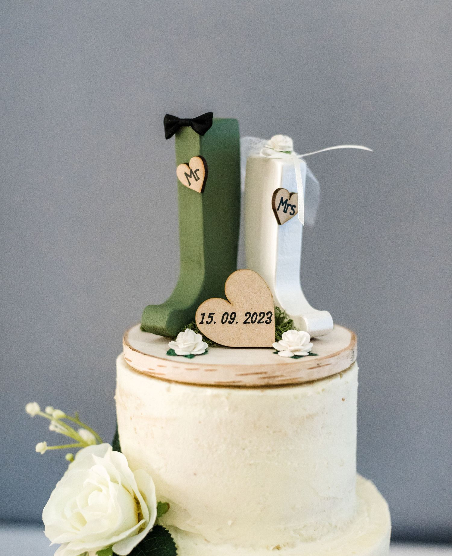 Wedding cake topper featuring green and white boots with heart detail and date.