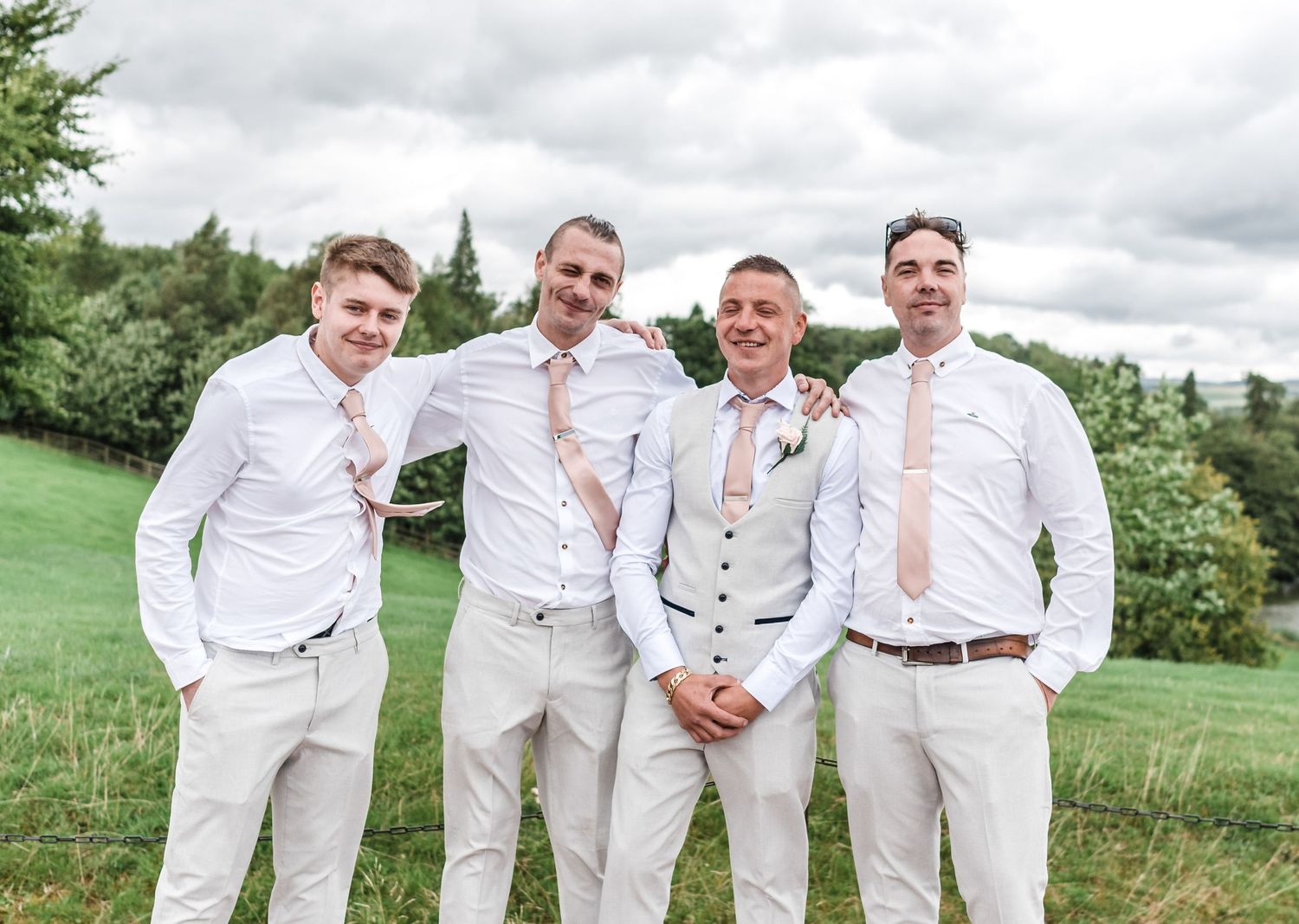 Groomsmen in coordinated white and beige attire pose on a grassy hill.