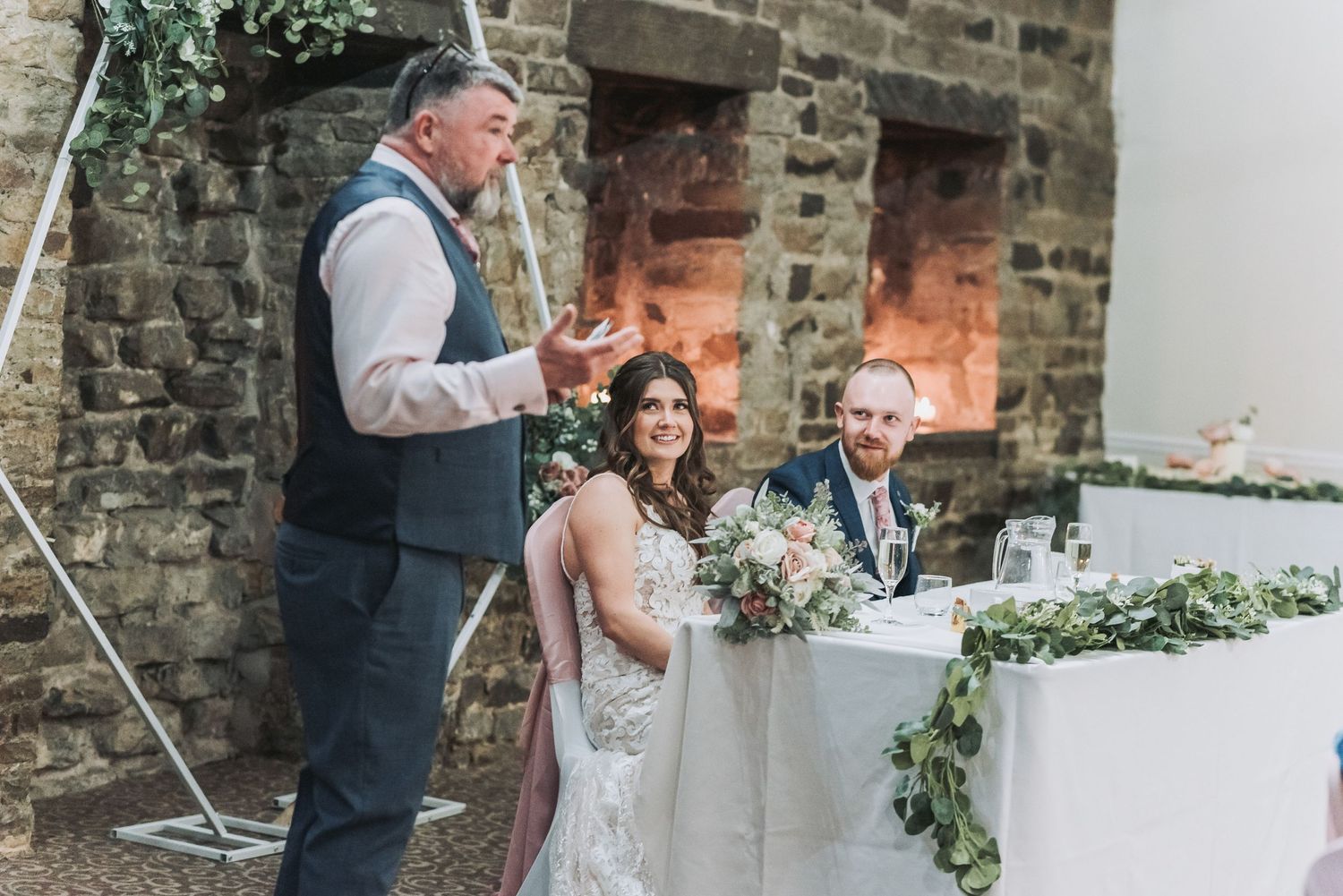 Wedding reception speech moment at rustic stone venue with floral decorations.