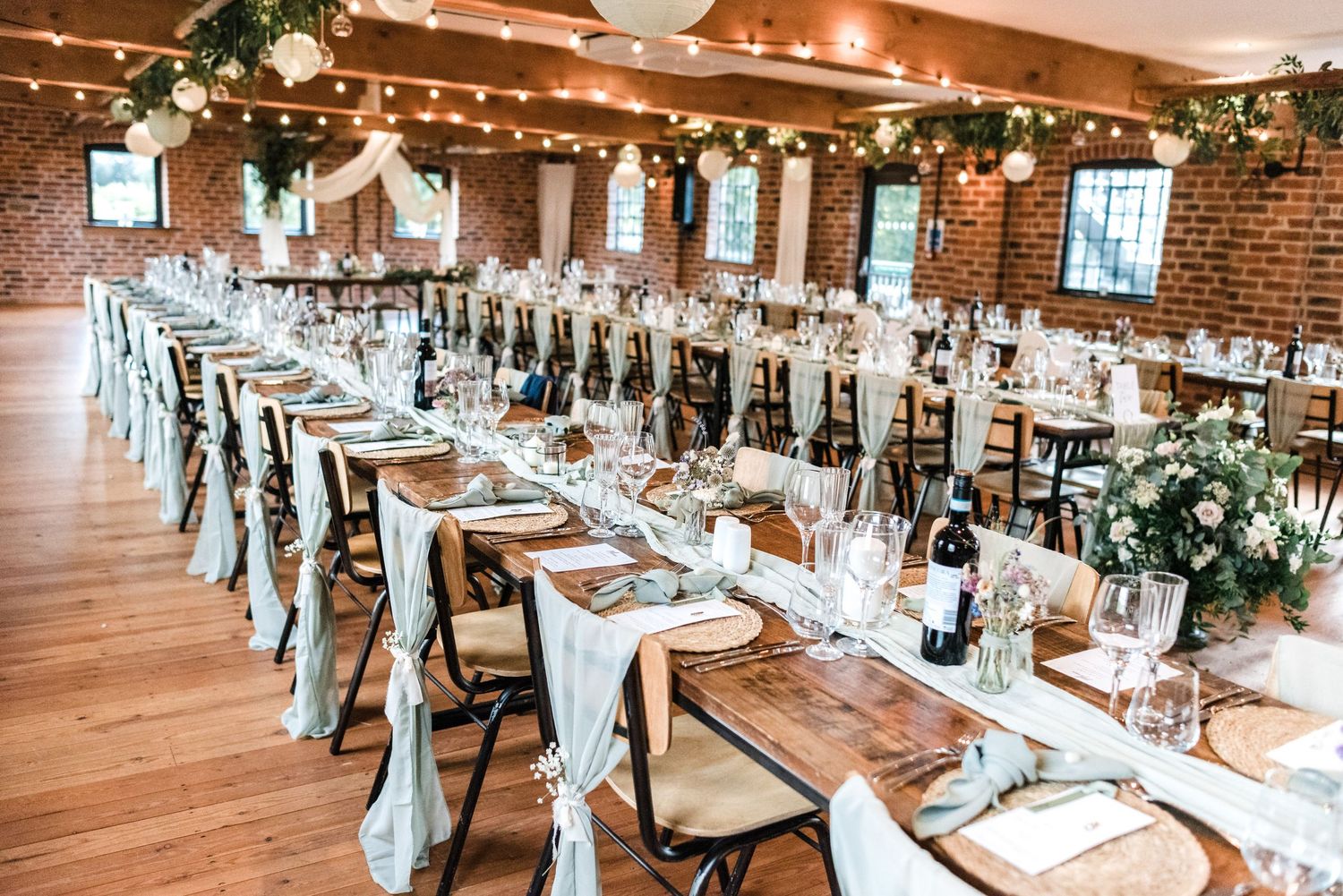 Long banquet tables with white linens and greenery in industrial-style brick wedding venue.