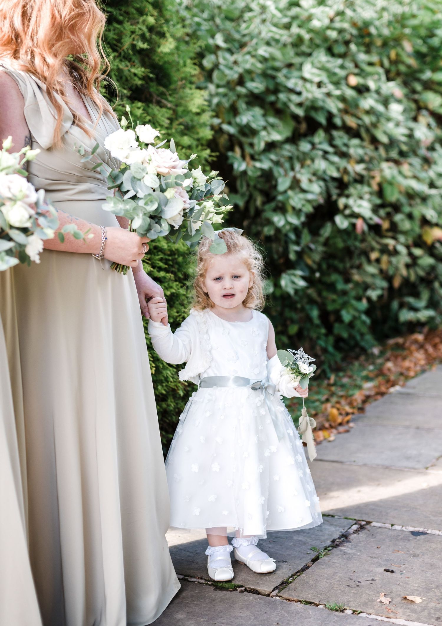 Floral wedding scene with bridesmaids in beige dresses and a small attendant in white.