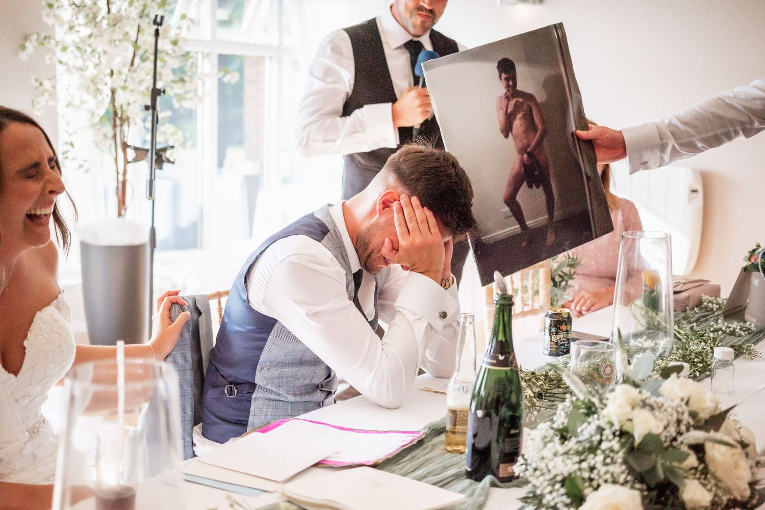 Emotional moment during wedding speeches with guests laughing and showing photos.