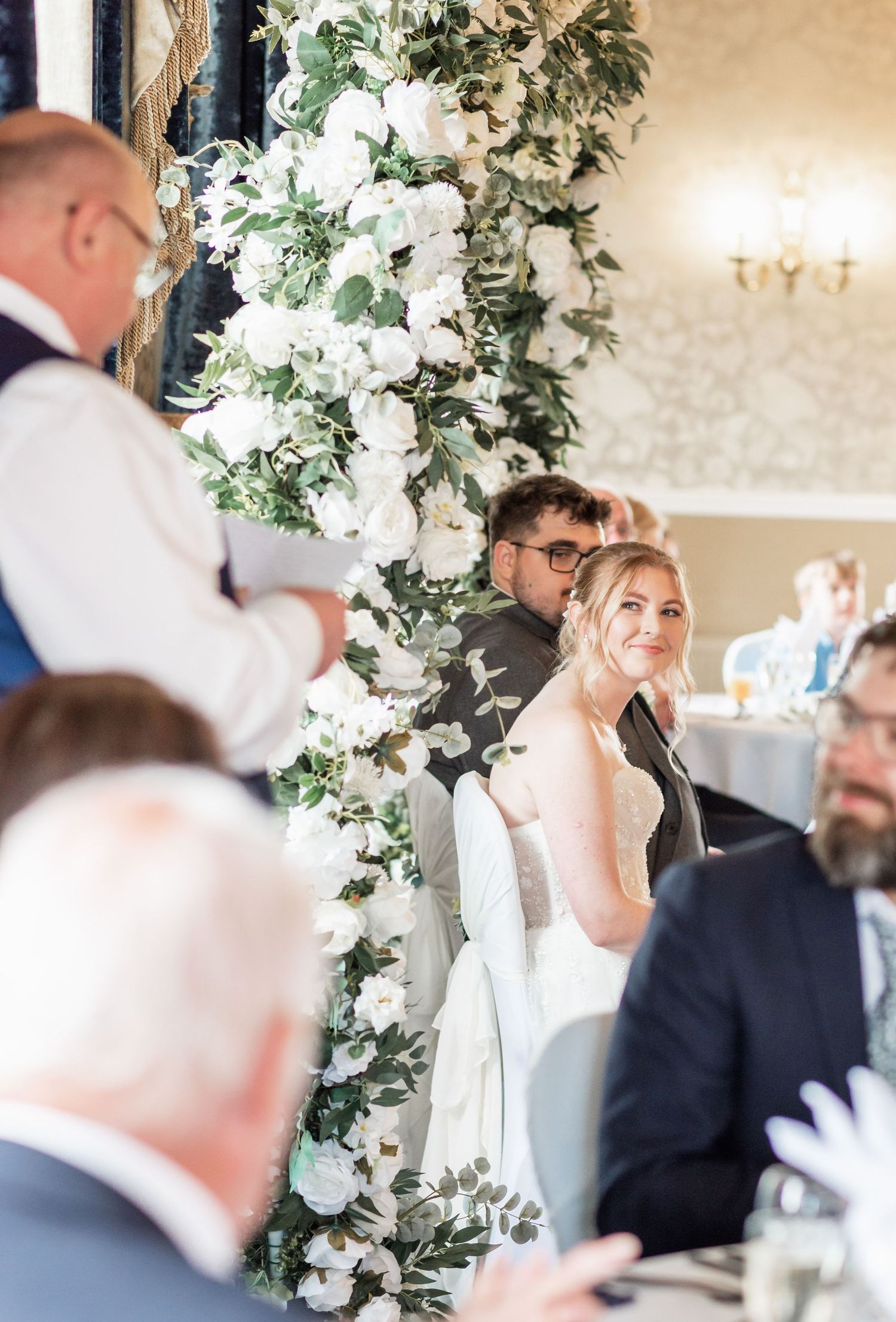 Elegant wedding reception with beautiful white floral arch and decorations in grand ballroom setting.