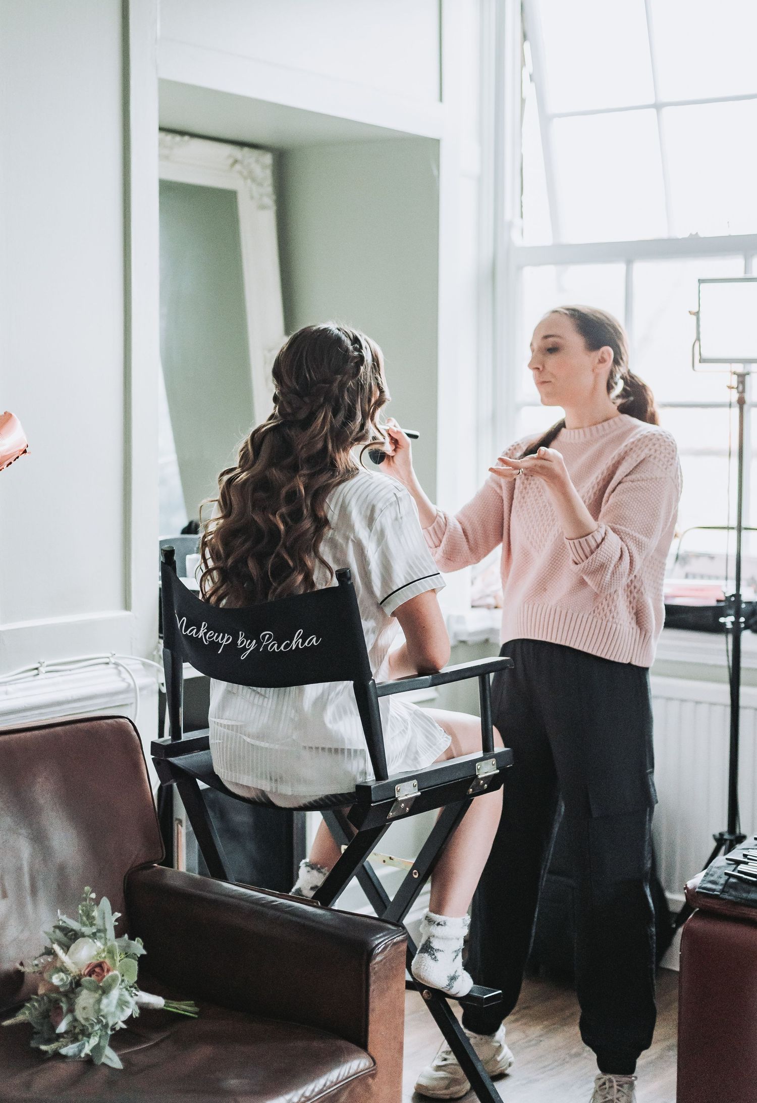 Behind-the-scenes wedding preparation showing makeup application in a bridal styling chair.