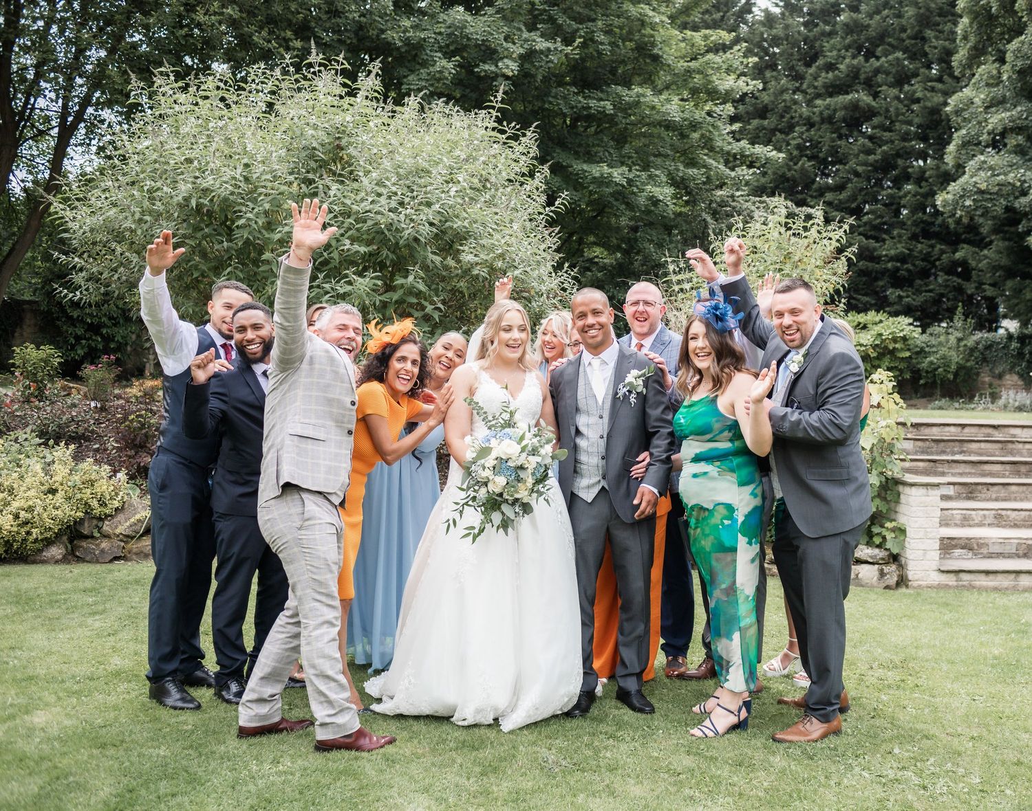 Wedding party members celebrate outdoors with enthusiastic poses and colorful attire.