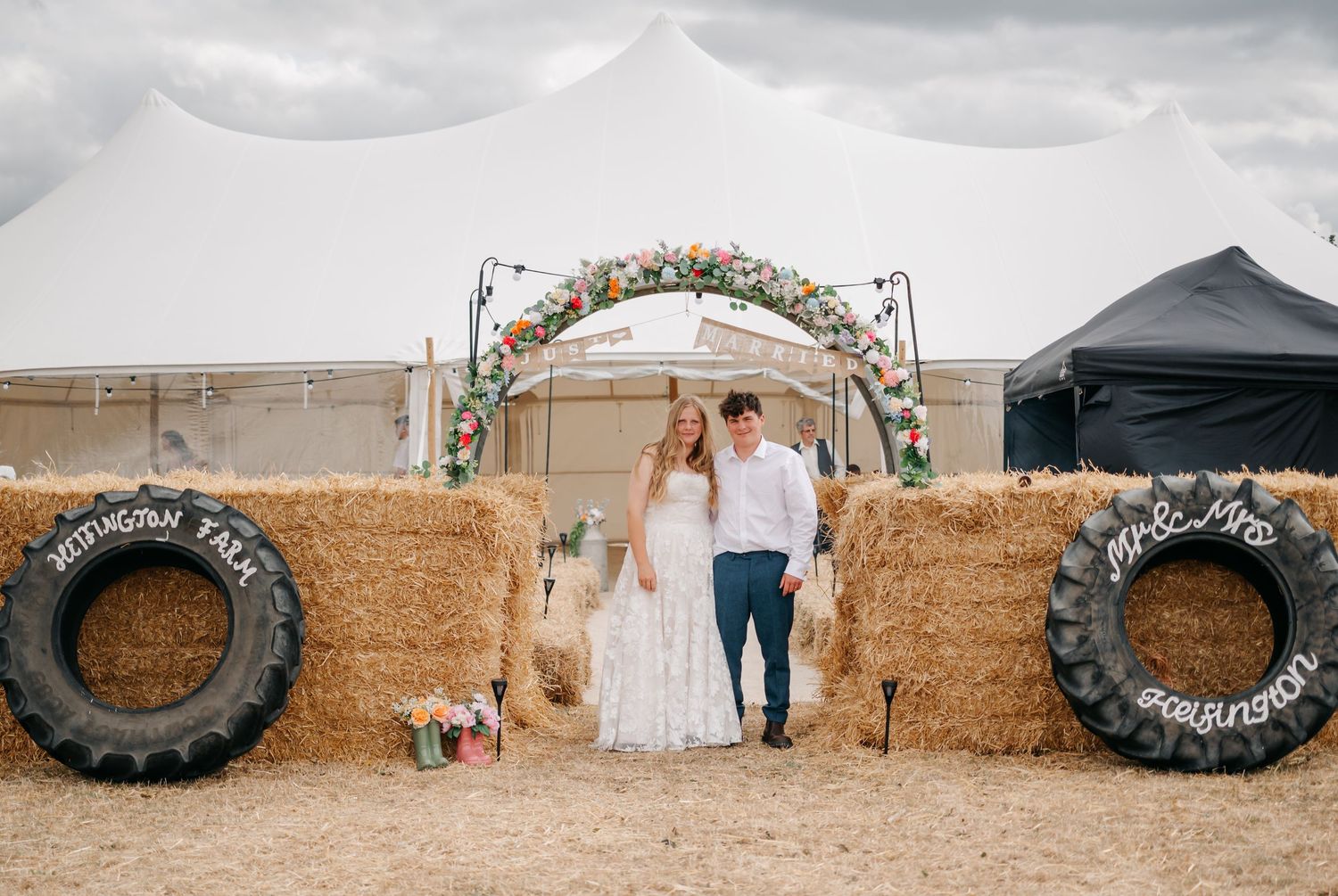 Wedding ceremony setup with rustic tire arch and hay bales in an outdoor farm setting.