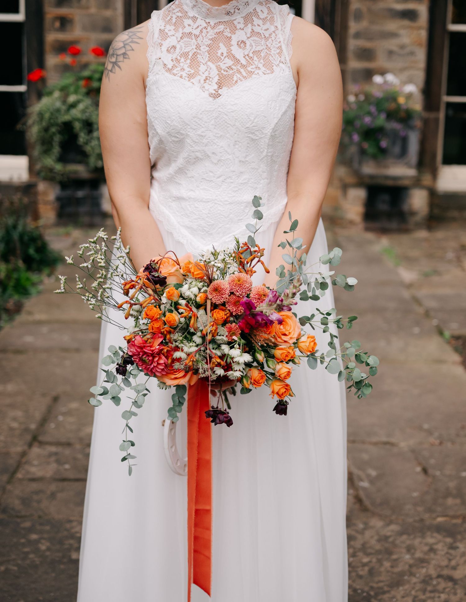 Close-up of bridal bouquet featuring orange and burgundy flowers with cascading ribbons.