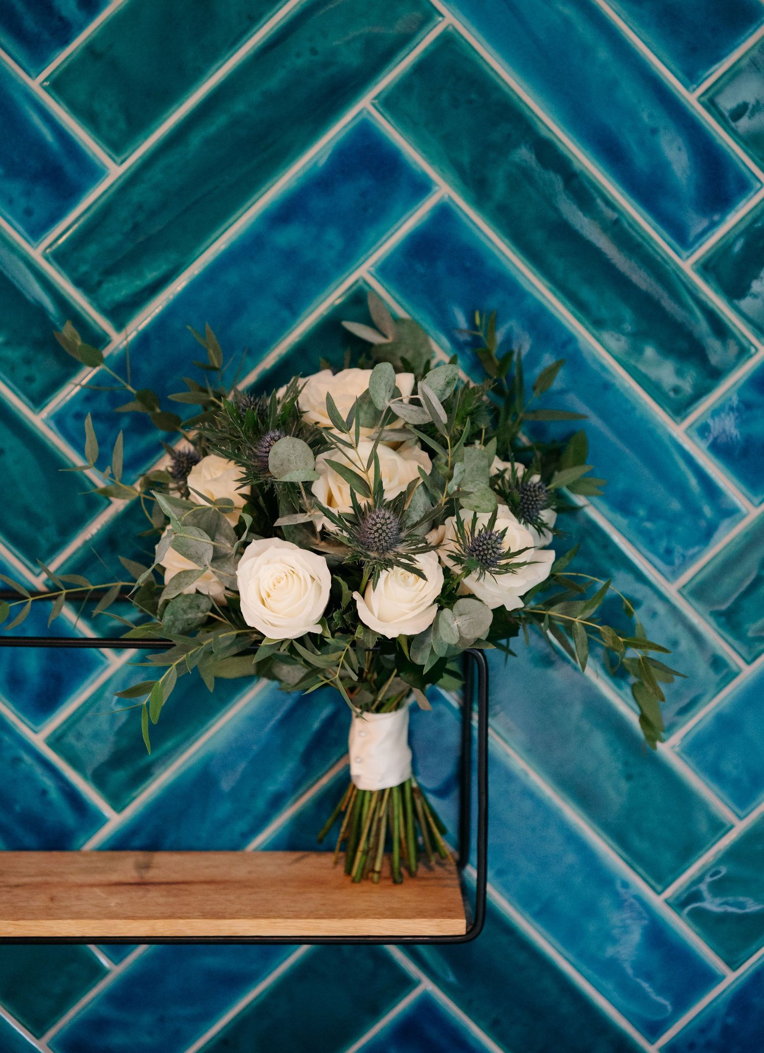 White roses and greenery arranged against vibrant blue herringbone tile backsplash.
